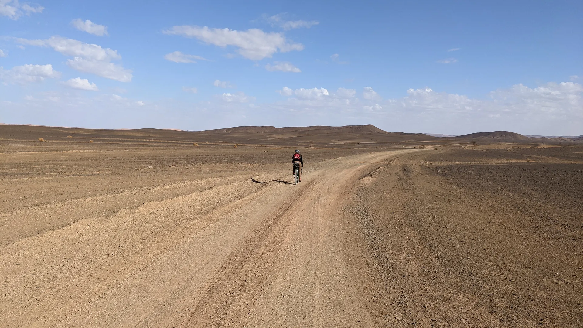 The image shows a person biking on a dirt road in a desert-like landscape.