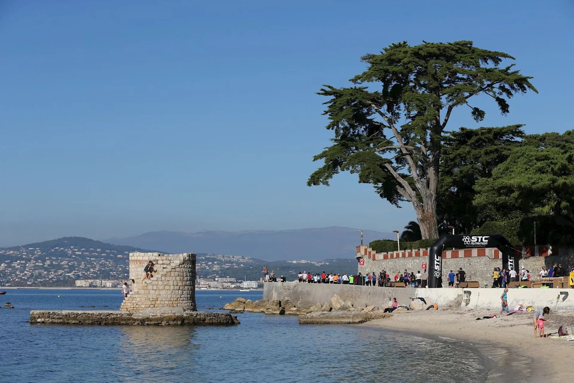 The image shows a coastal scene with a bright blue sky and calm sea. On