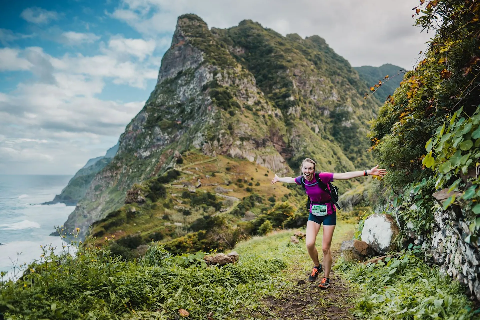 The image shows a person trail running along a scenic coastal path. The individual appears