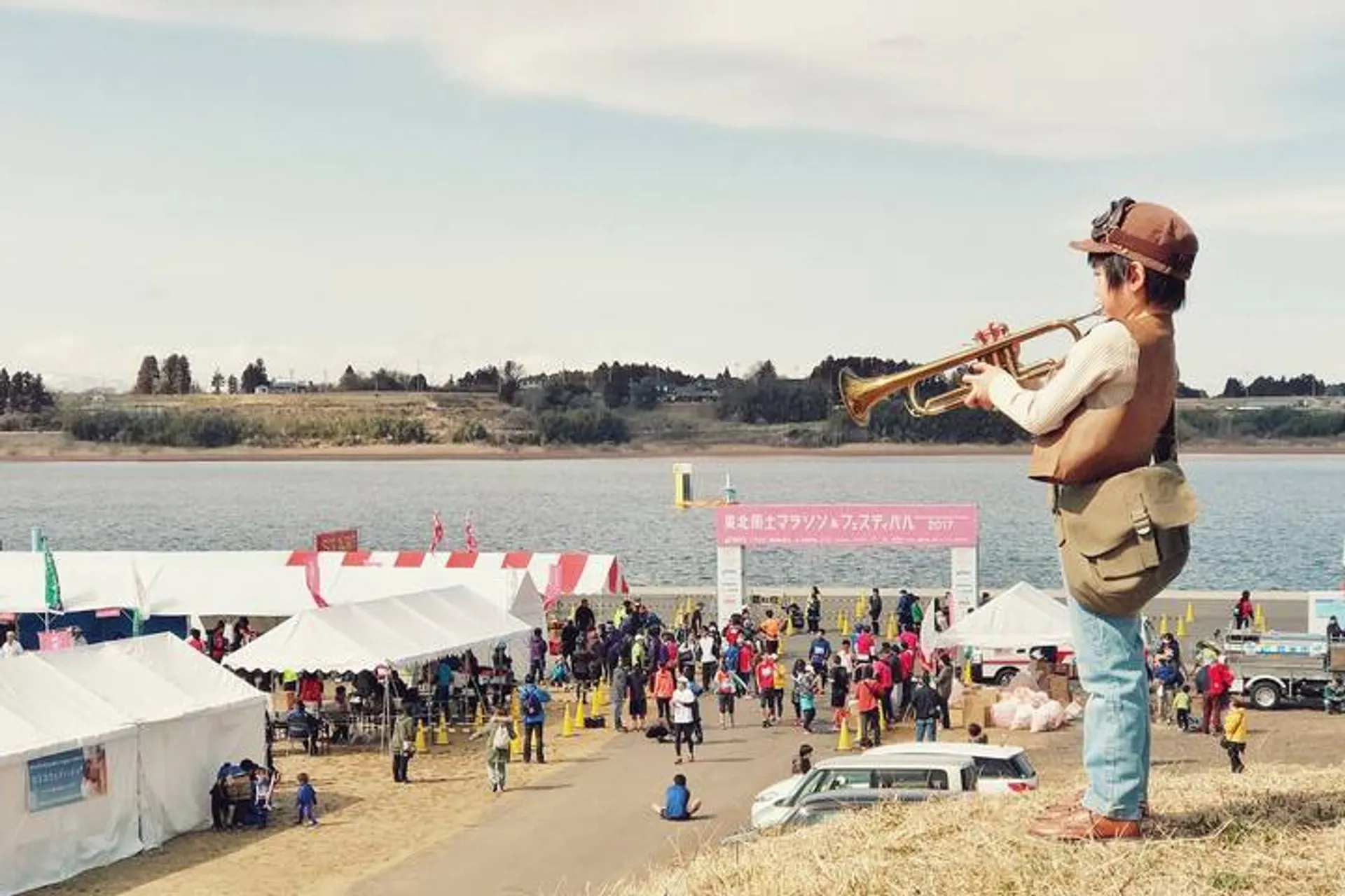 The image shows an outdoor scene with a person in the foreground playing the trumpet.