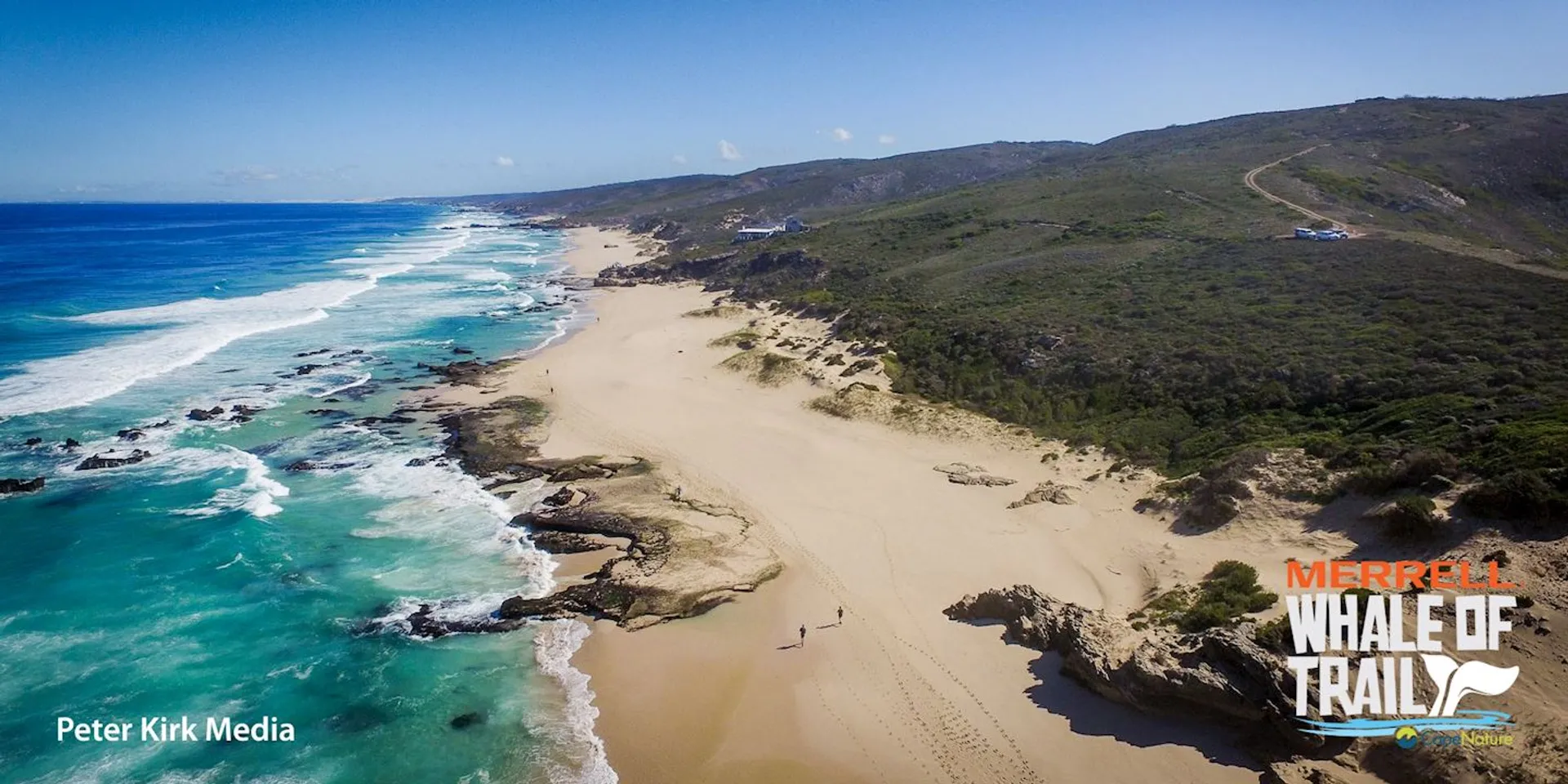 The image shows an aerial view of a coastal landscape featuring a sandy beach with waves