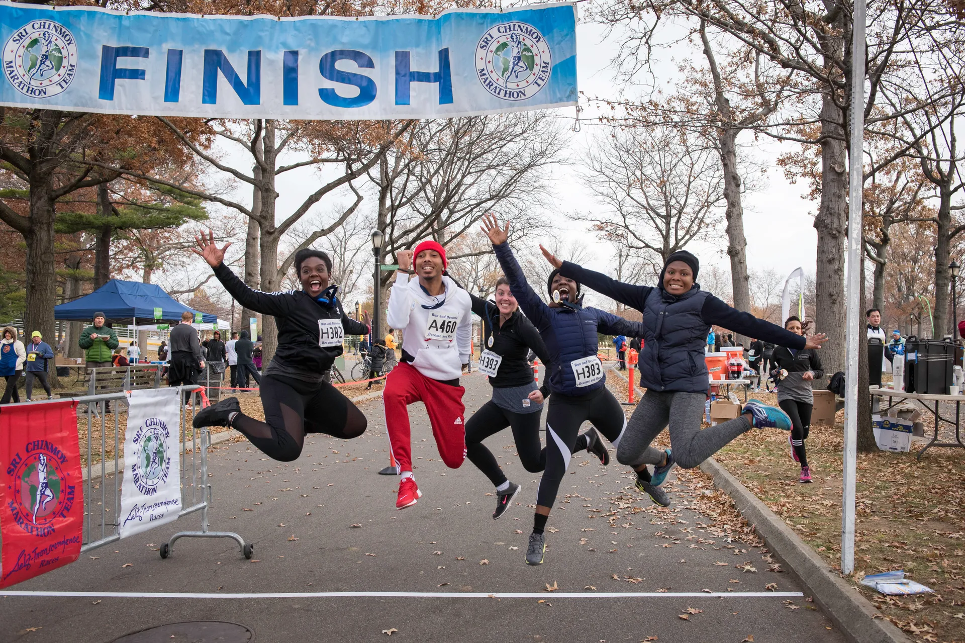 The image shows four people celebrating as they jump across a finish line at a race