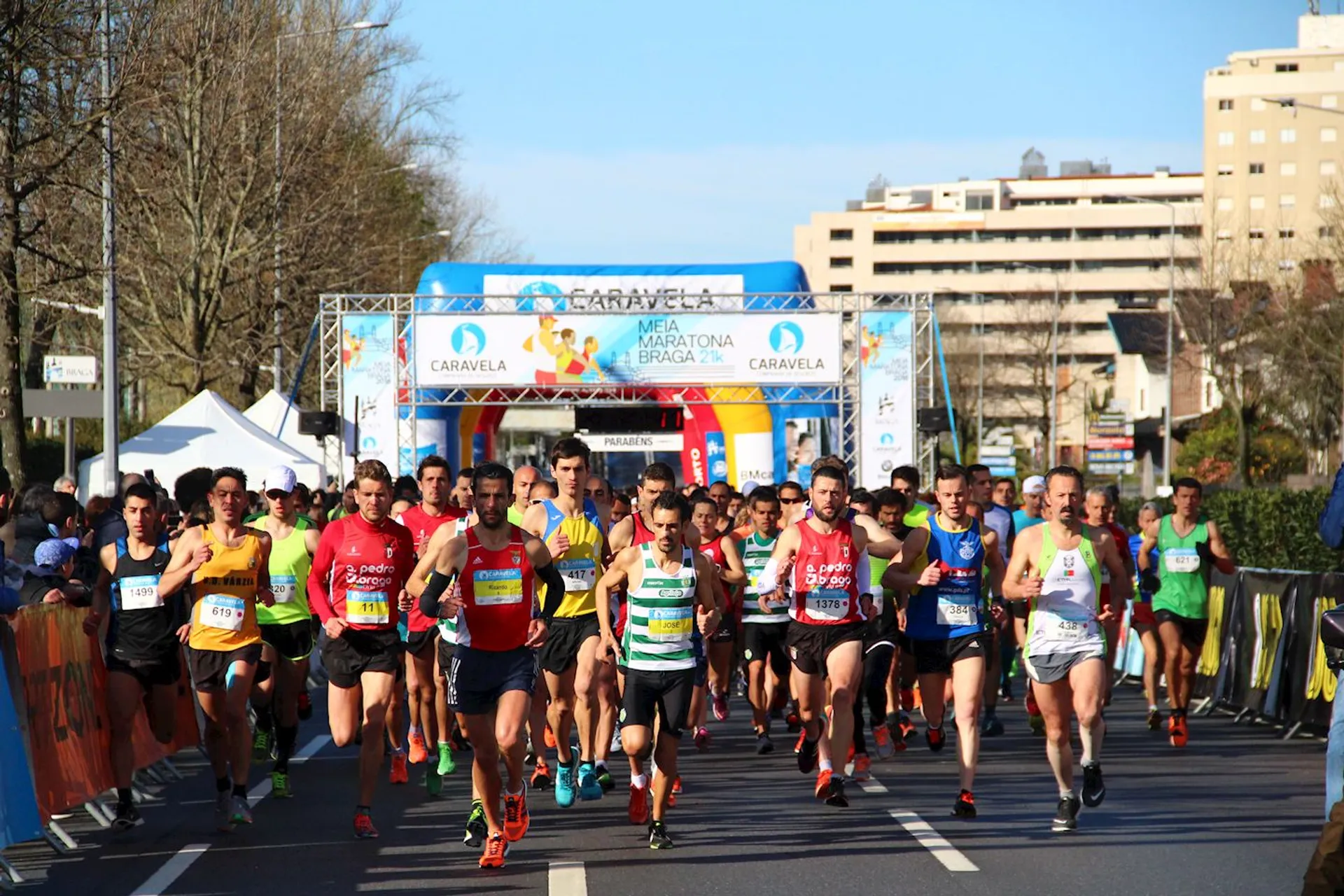 The image shows a group of runners at the starting line of a marathon or road