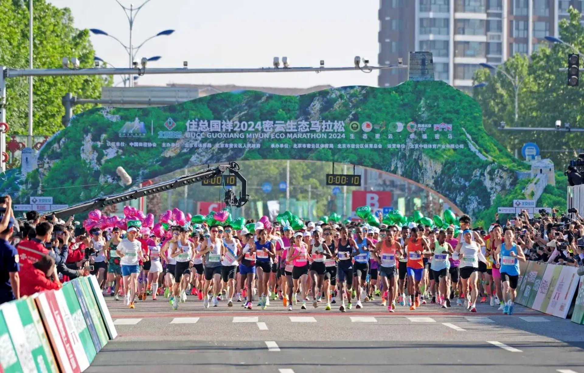 The image shows a large group of runners at the start of a marathon. The race appears to be the "Guiyang Eco Marathon 2024," as indicated by the banner overhead. Spectators and photographers line the sides of the street, capturing the event.