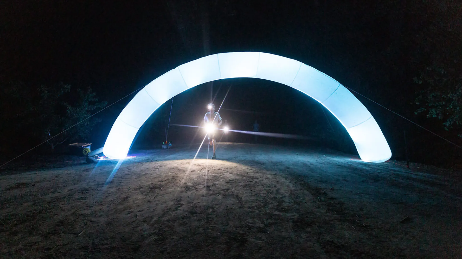 The image shows a large, illuminated arch structure at night. Beneath the arch