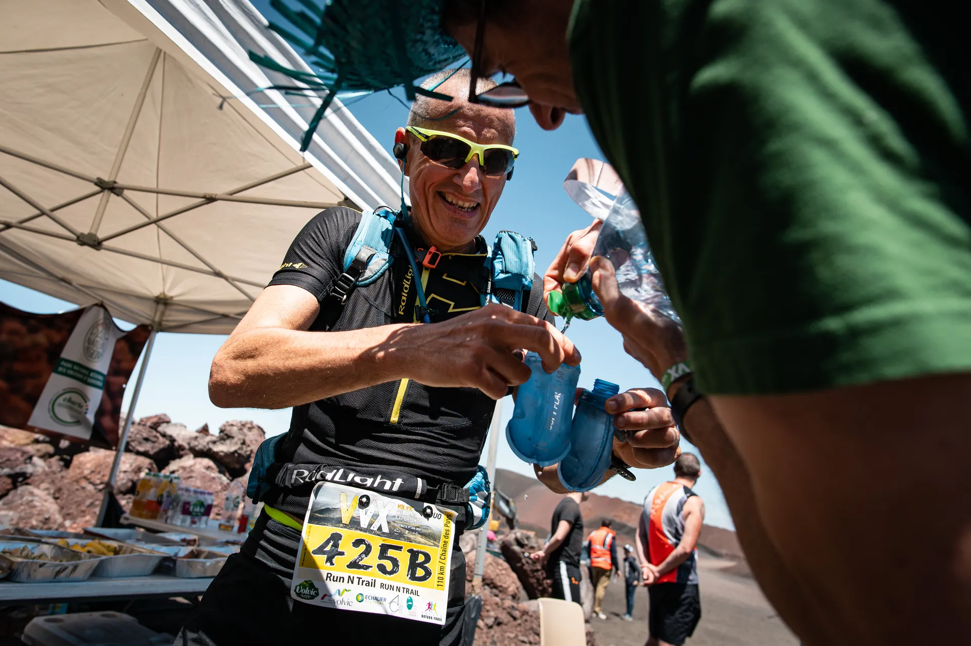 The image shows an outdoor scene where a runner wearing sunglasses, a hydration pack,