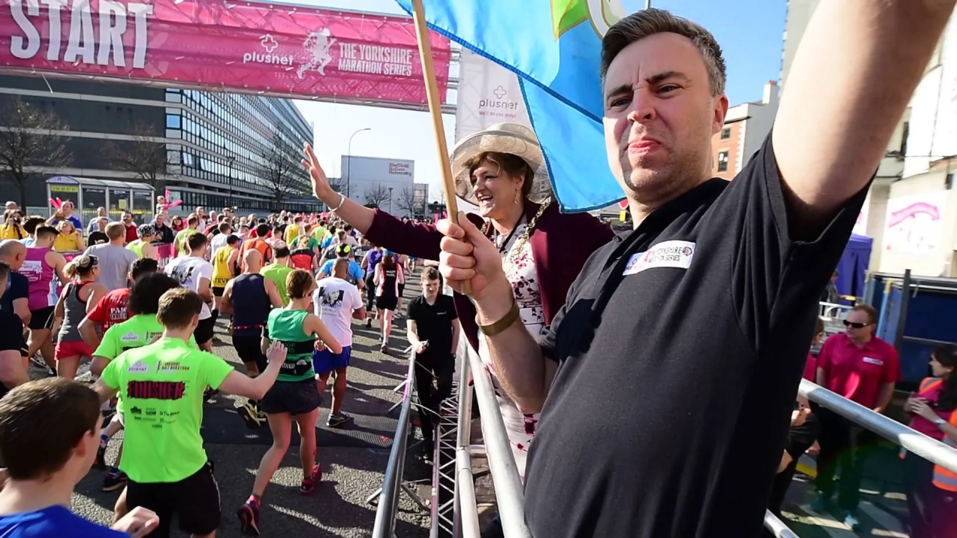 The image shows a man in the foreground taking a selfie, with his arm extended