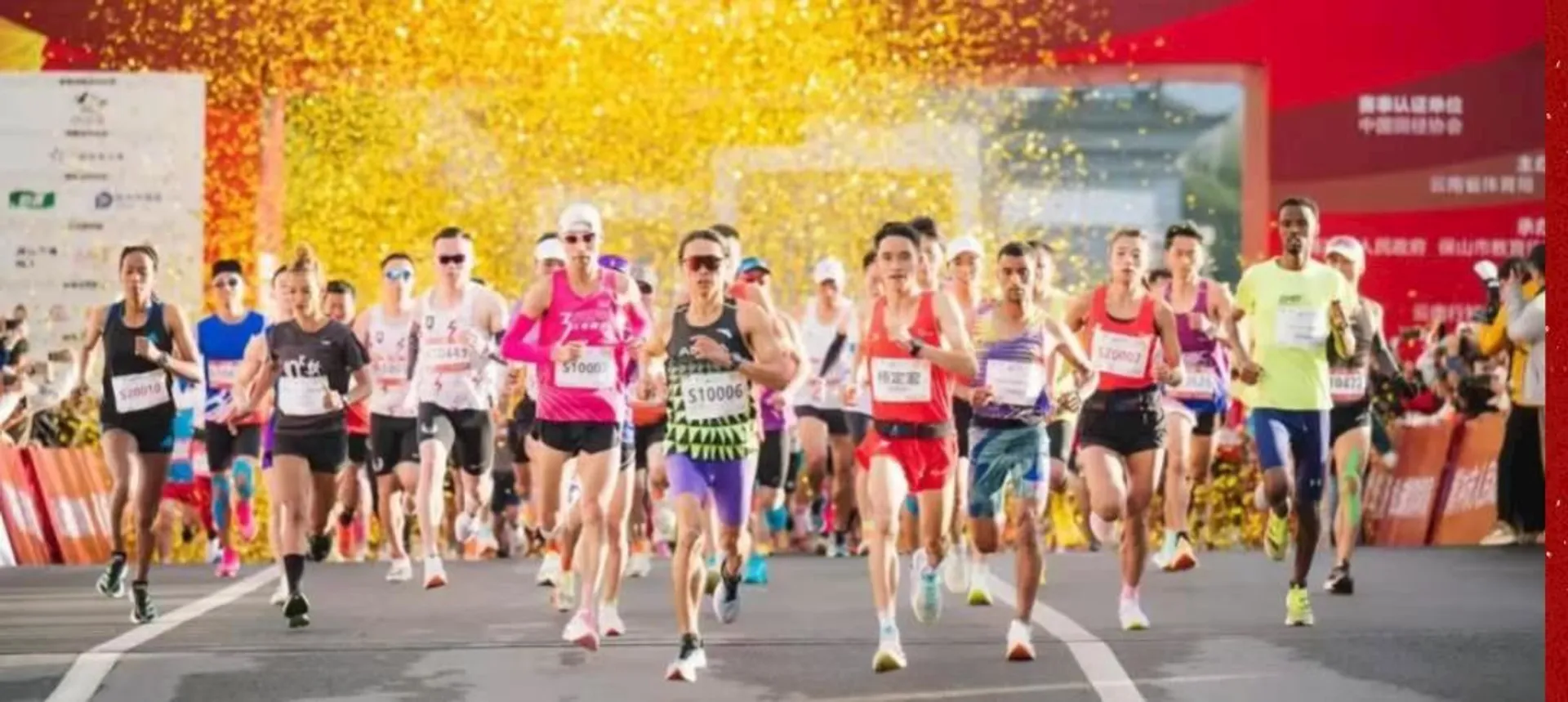 This image shows a group of runners participating in a race or marathon. The runners are on a road, and there are yellow confetti or streamers in the background, which suggests a festive or celebratory atmosphere. Some participants are wearing bib numbers and athletic gear.