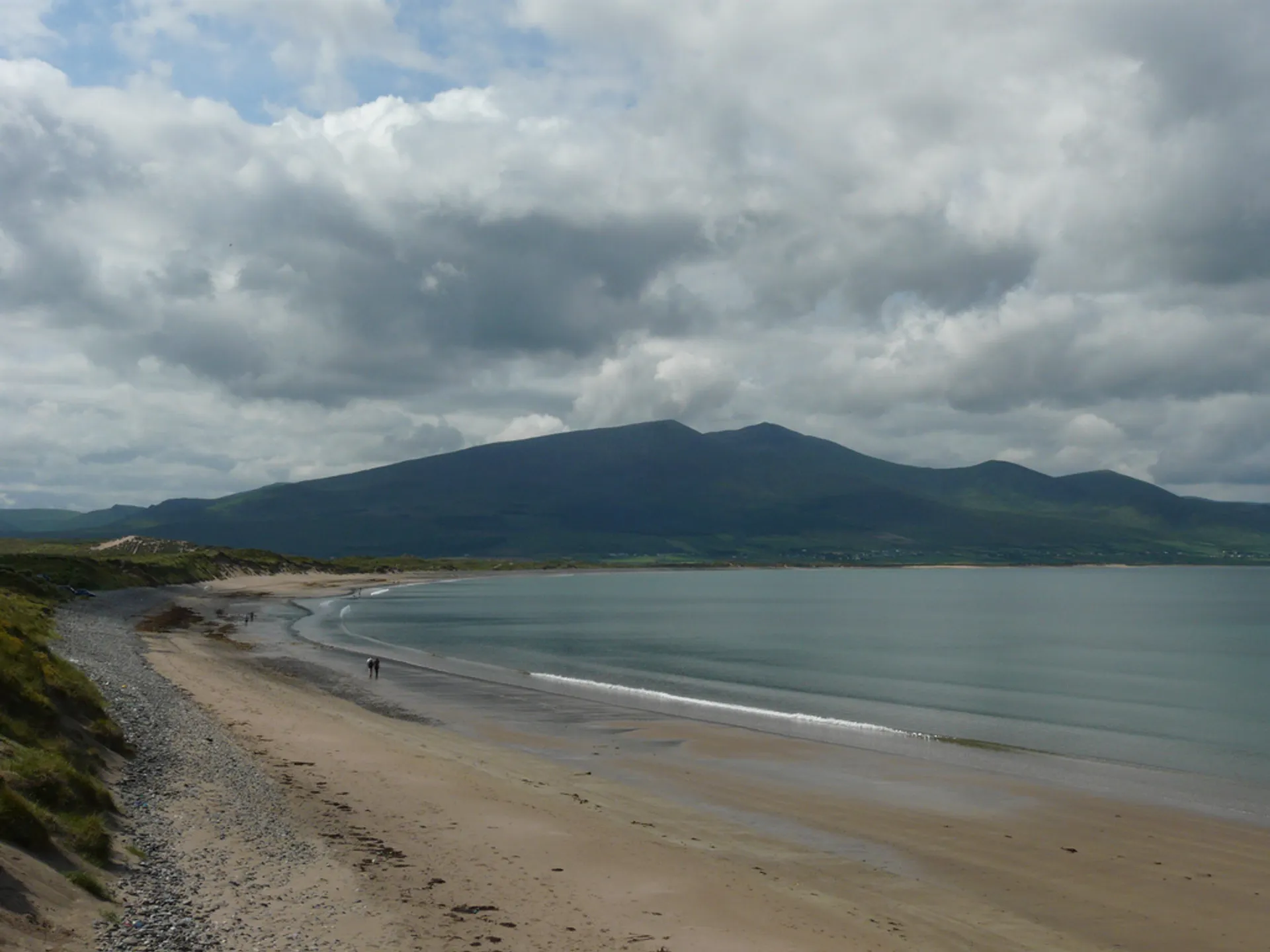The image shows a scenic landscape featuring a wide beach with a curved shoreline. The