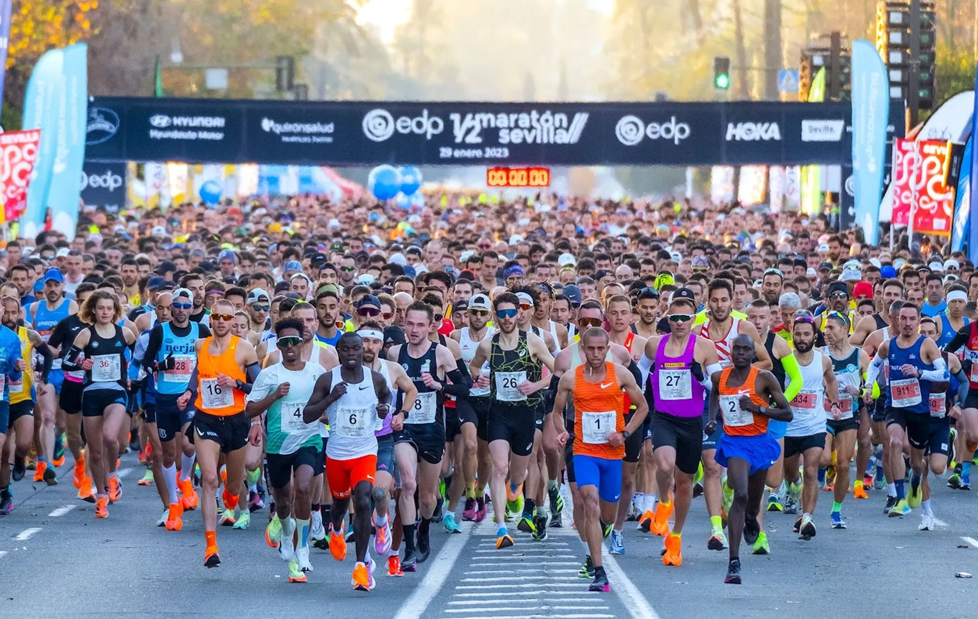 The image shows a large group of runners at the start of a half-marathon