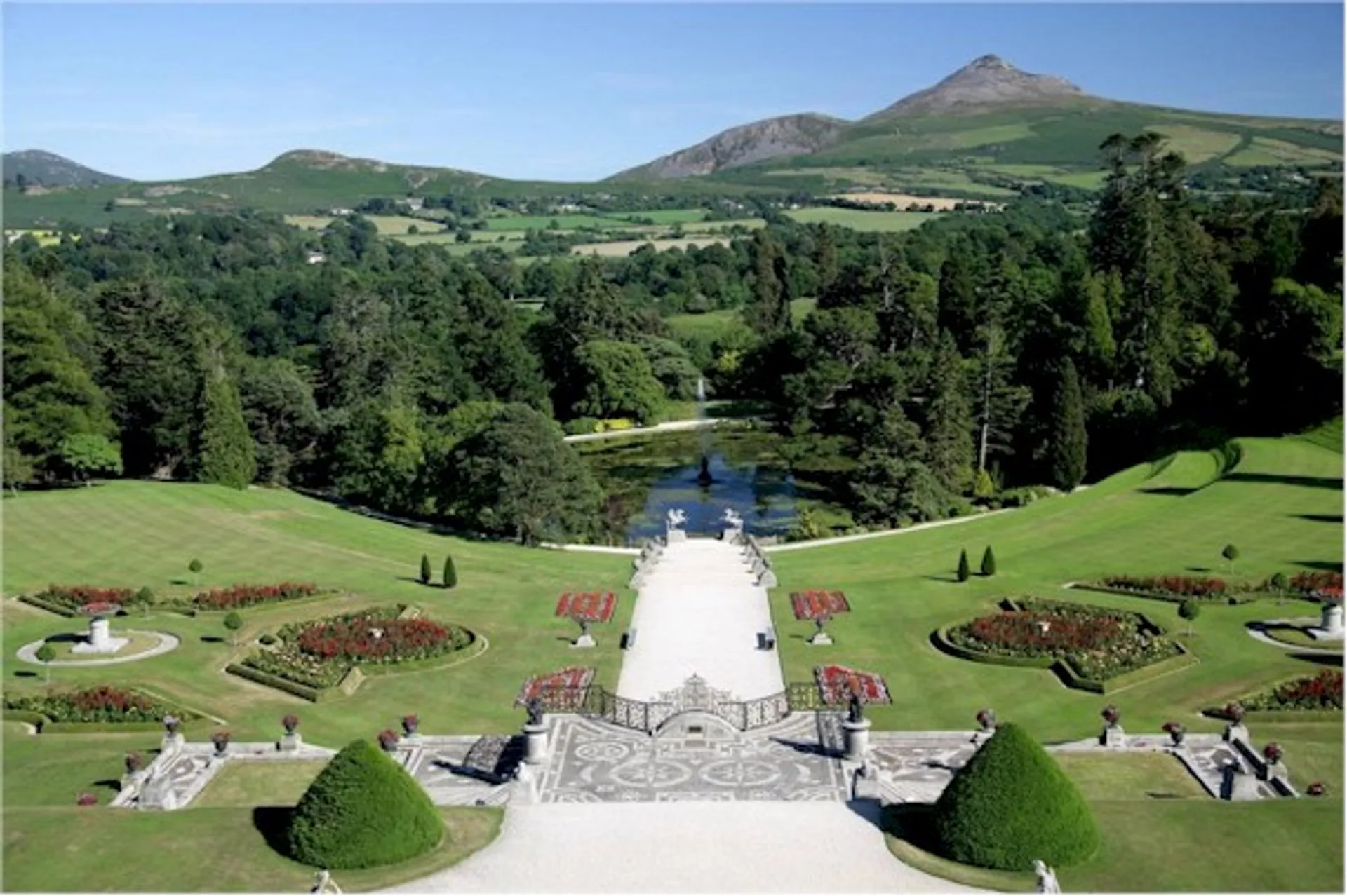 The image depicts a formal garden with manicured lawns and geometric flower beds,