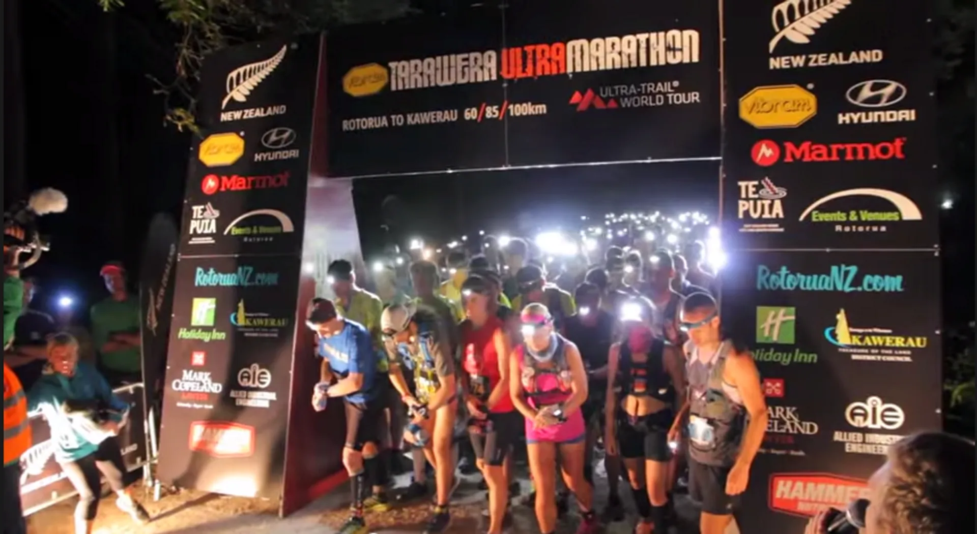 The image depicts a nighttime scene at the starting line of an ultramarathon race
