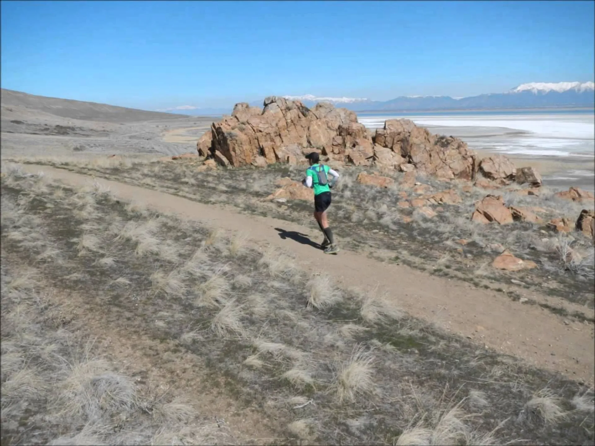 The image shows a person running on a trail in a natural setting. The runner