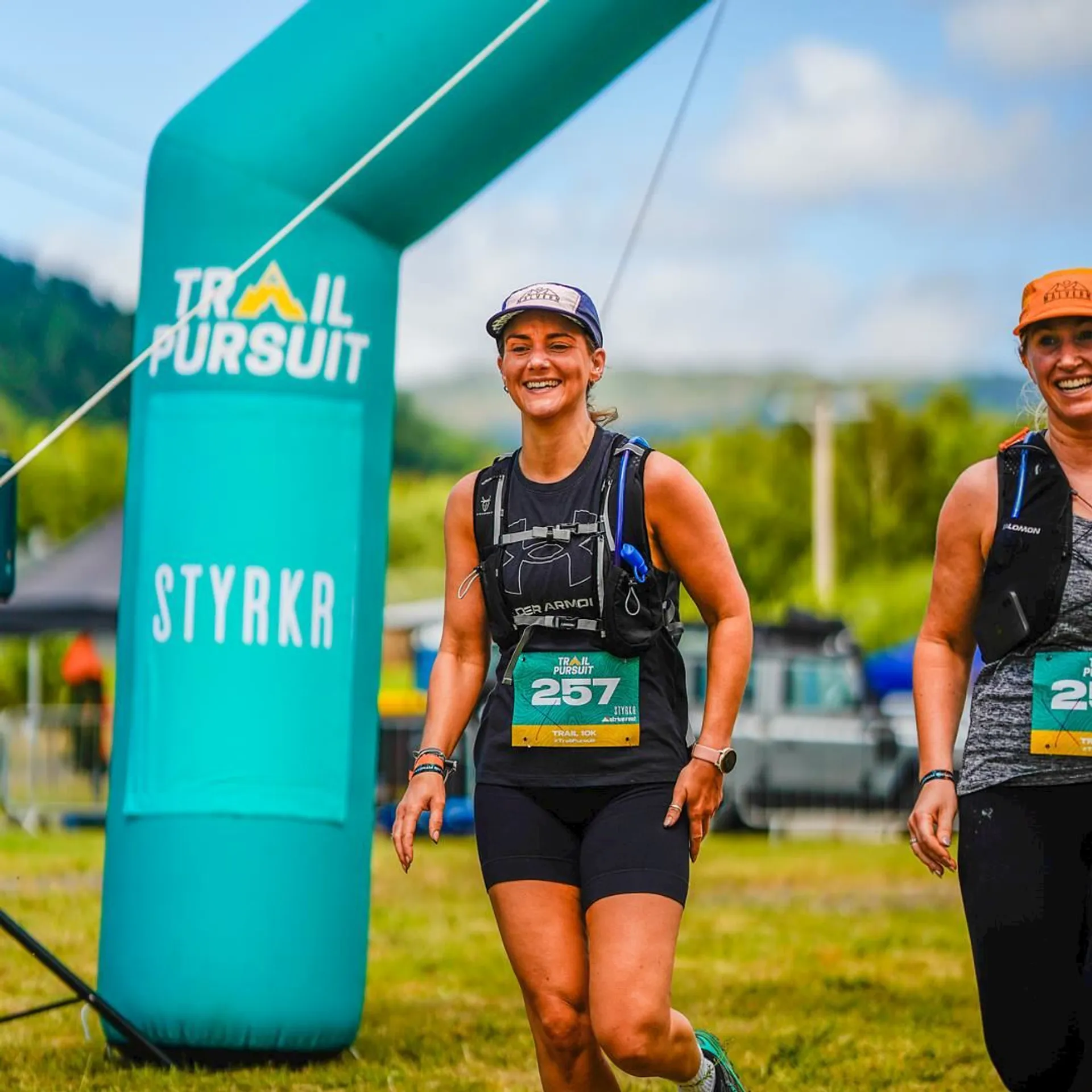 The image shows two women participating in a running event, likely a trail race given