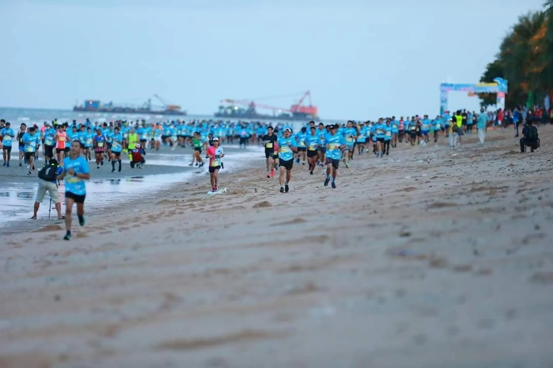 The image shows a large group of people participating in a running event on a beach