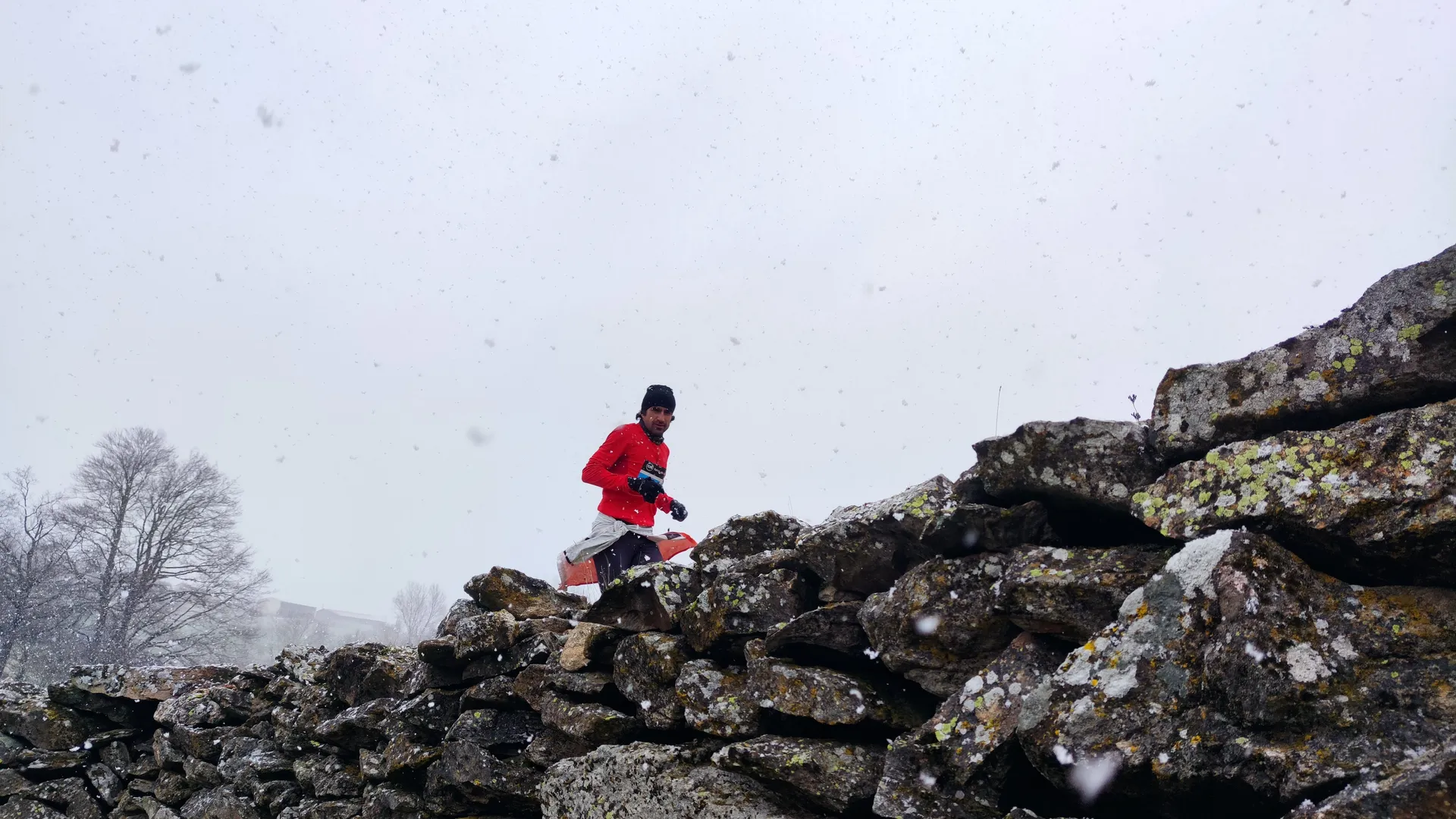 The image shows a person wearing a red jacket and black pants running on a rocky