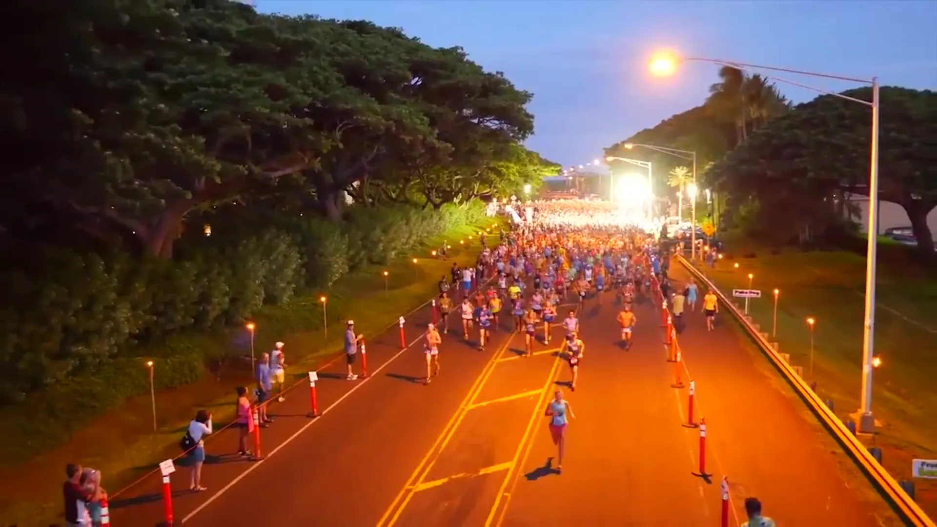 The image features a large group of runners participating in a road race during twilight or