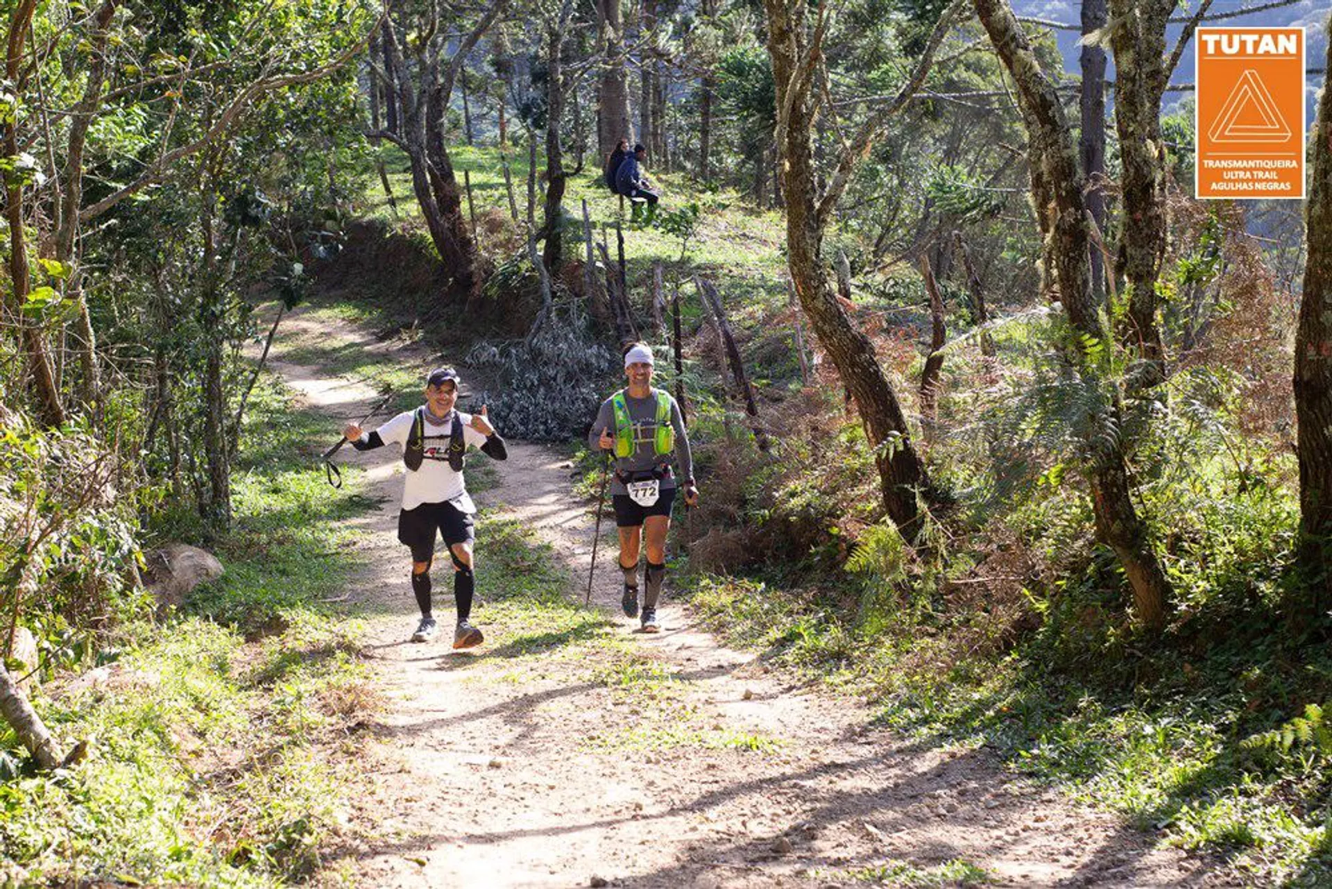 The image depicts two individuals participating in a trail running event. They are running on