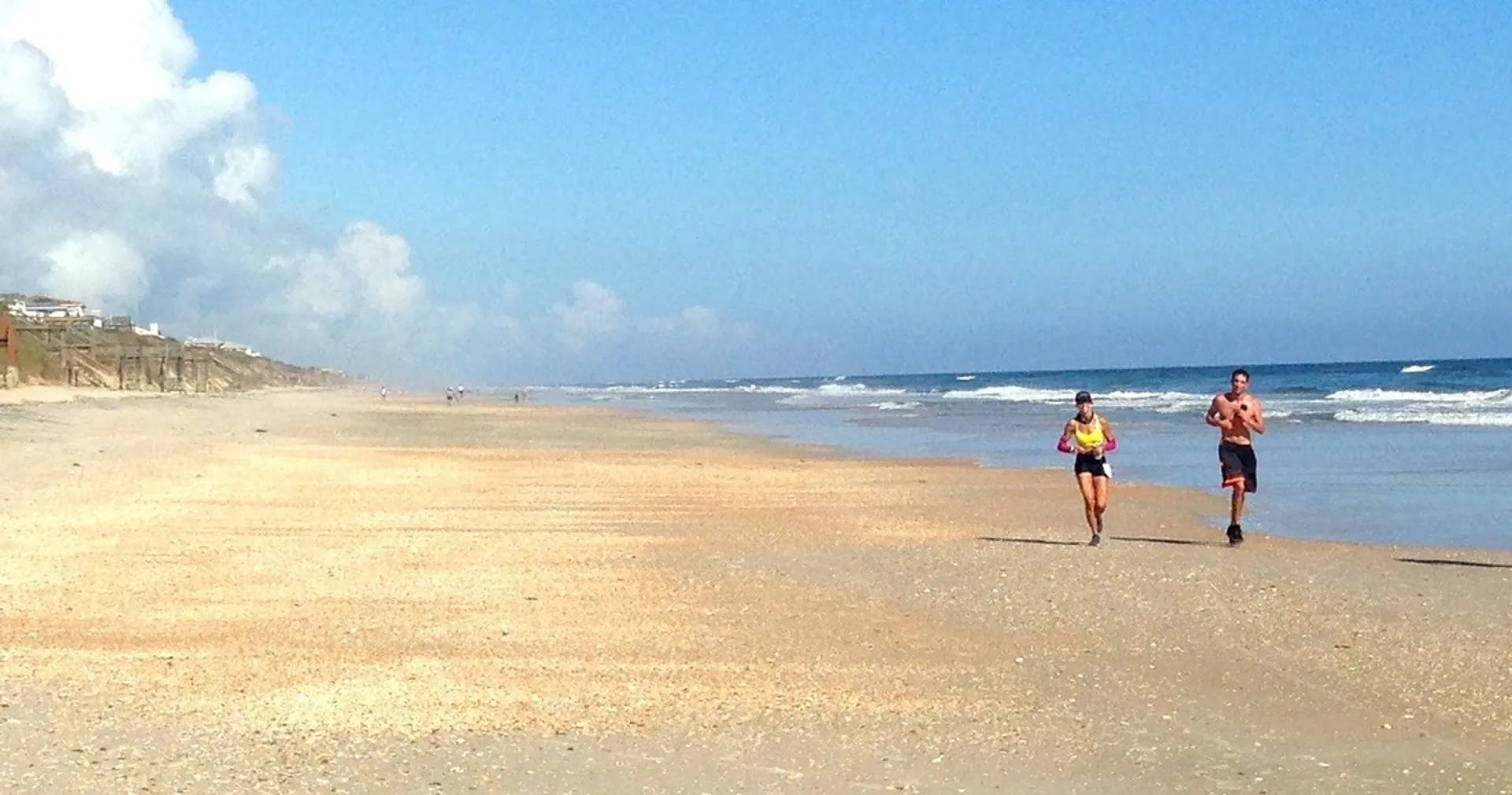 The image shows two people jogging on a sandy beach. The ocean is to their