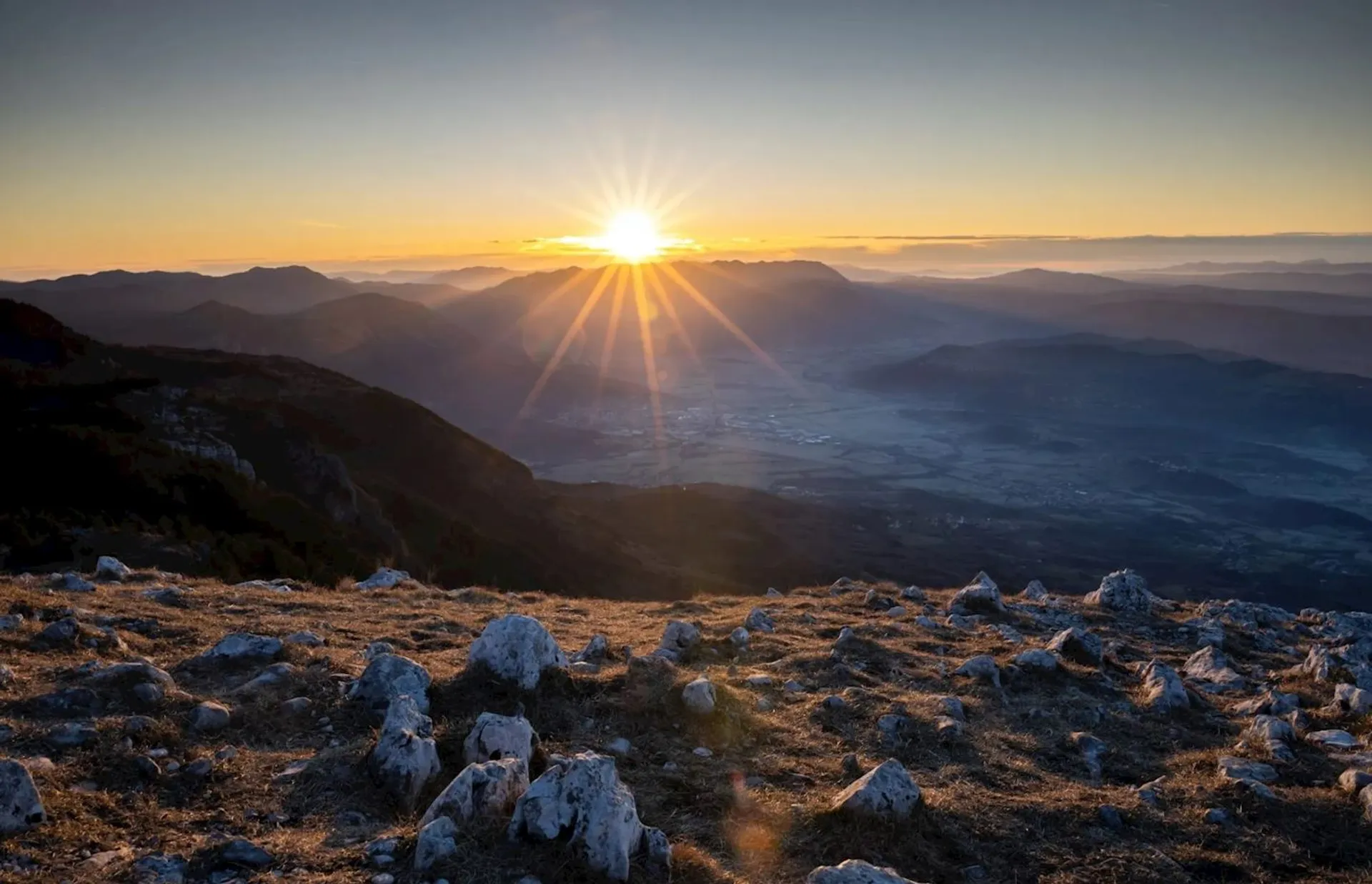 This image features a stunning sunrise over a mountainous landscape. The sun is prominently