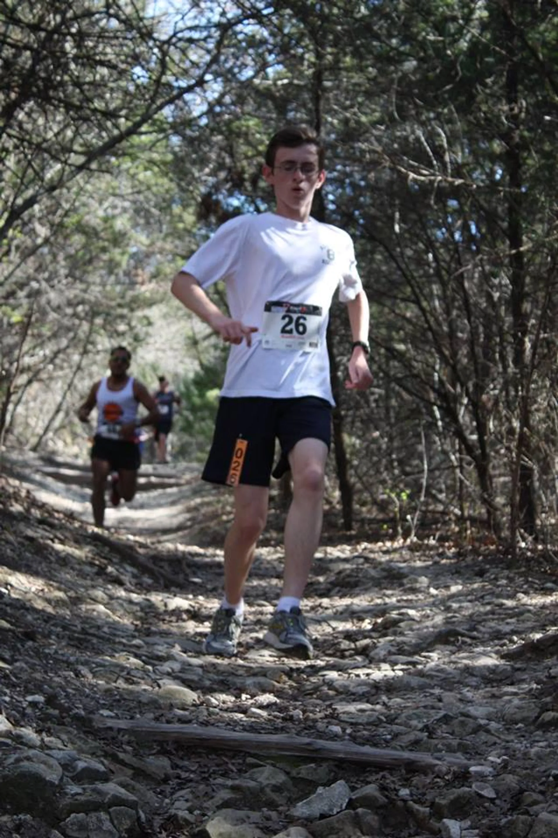 The image shows a runner wearing a white t-shirt with a bib number (26