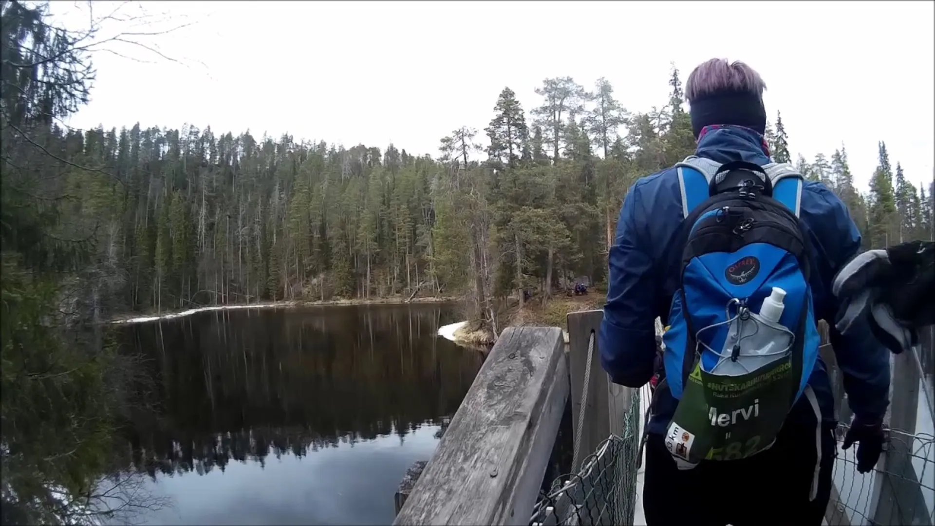 The image shows a person from behind standing on a wooden bridge over a body of