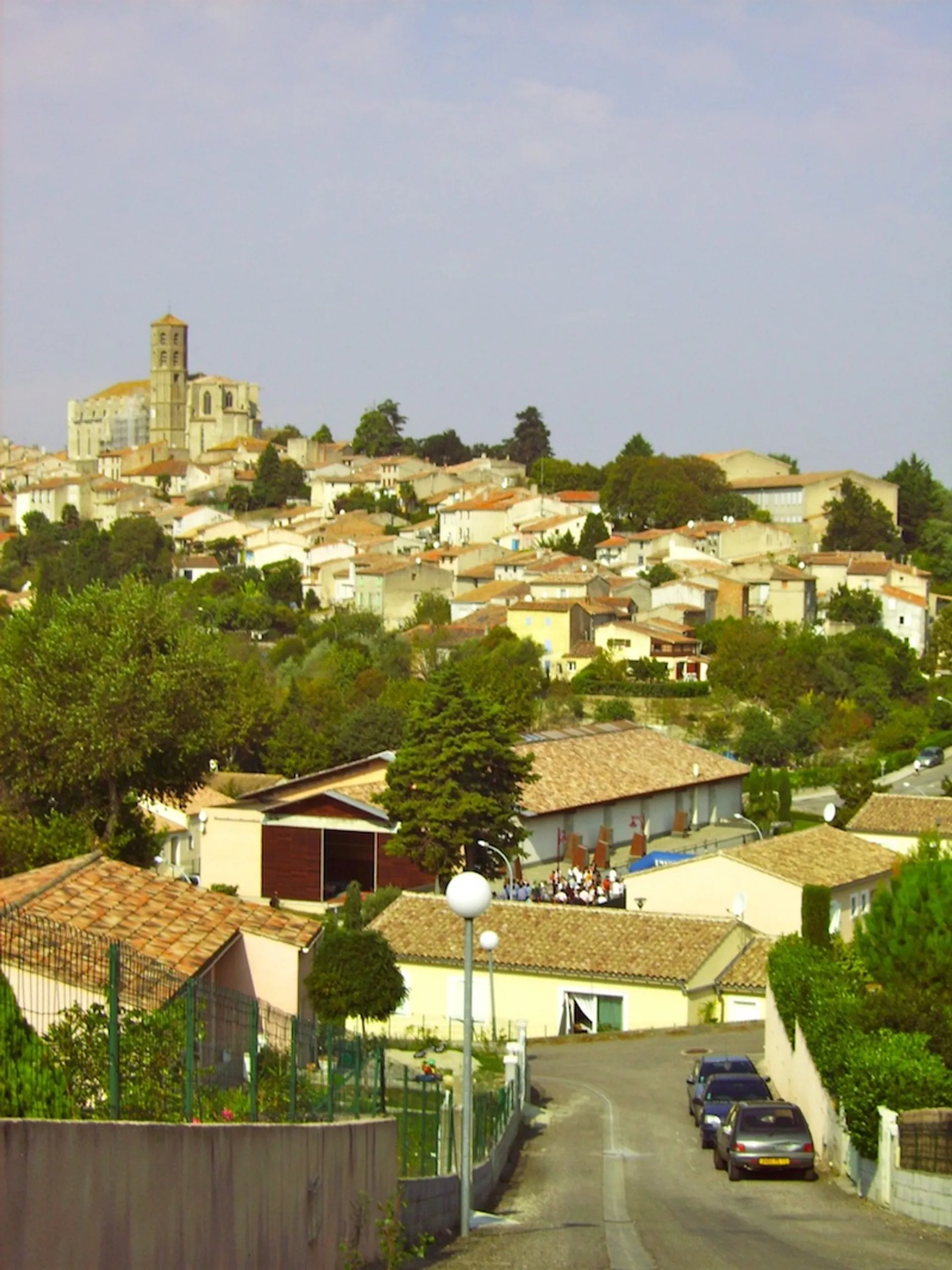 The image depicts a picturesque hilltop village under a clear sky. The village is