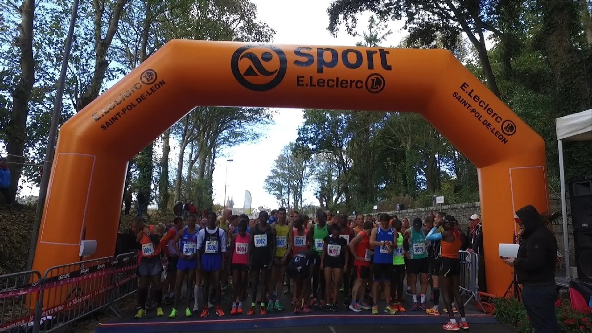 The image shows a group of runners lined up at the starting line under a large