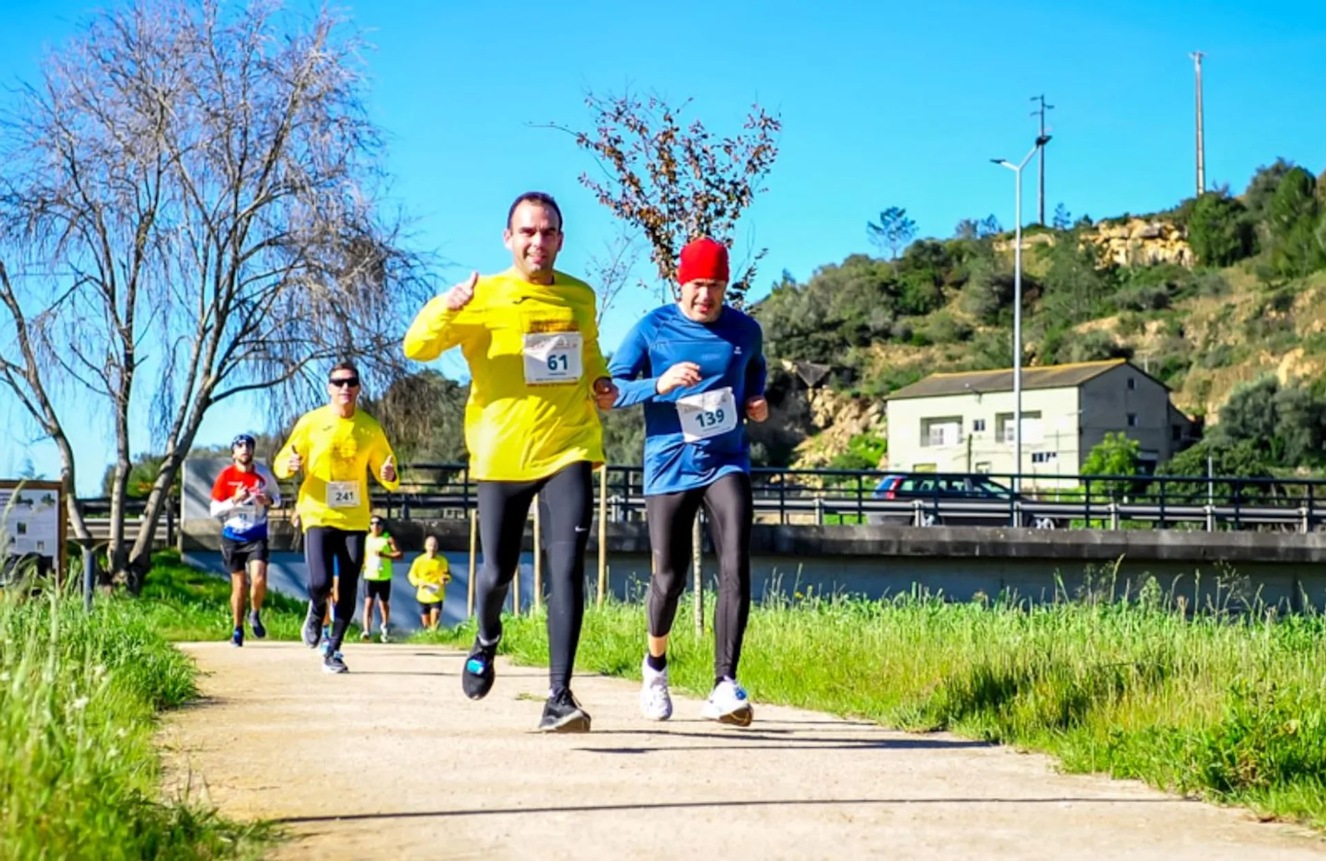 The image depicts several people participating in a running event or race on a sunny day
