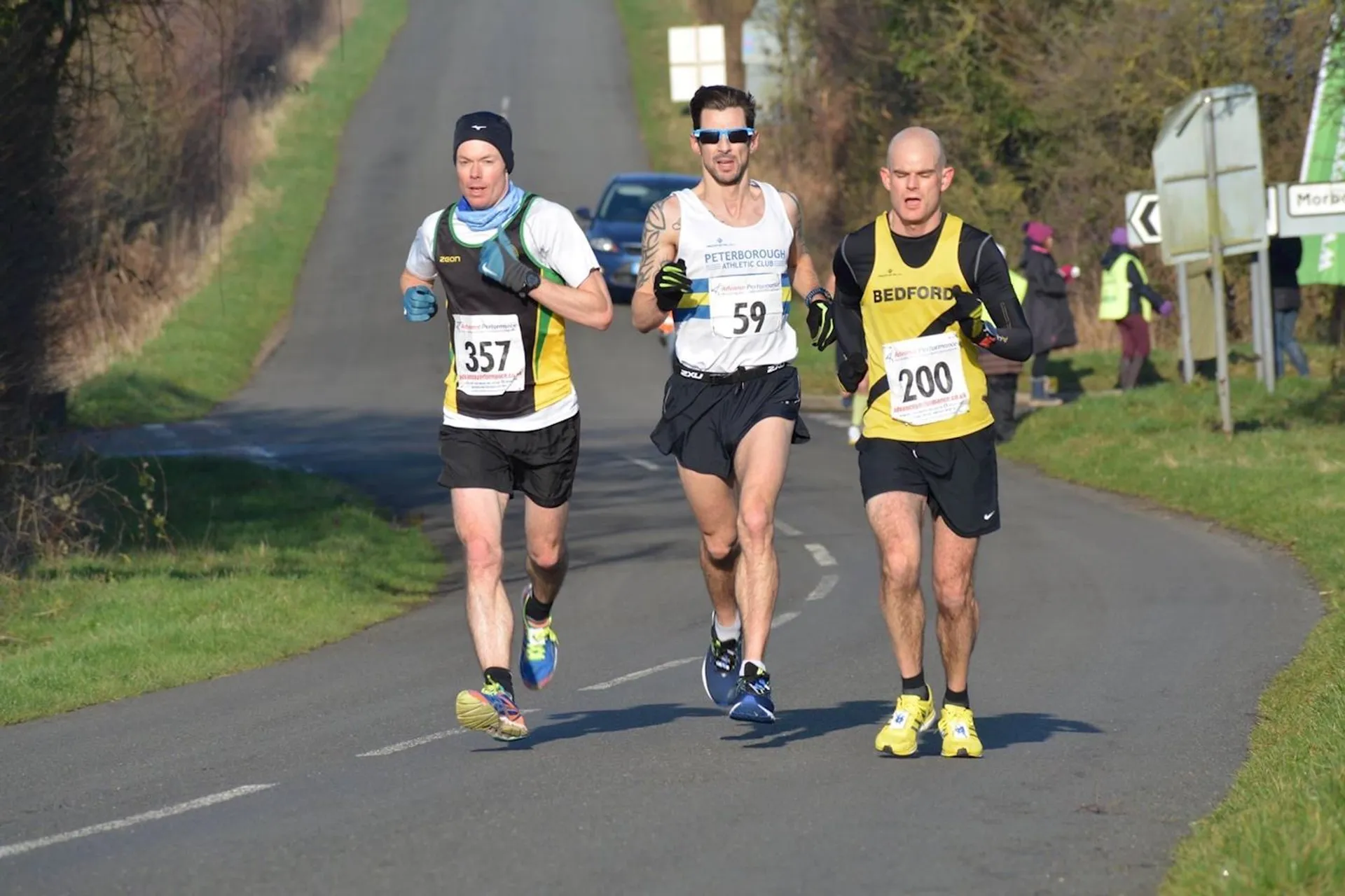 The image shows three male runners participating in a road race. They are wearing athletic