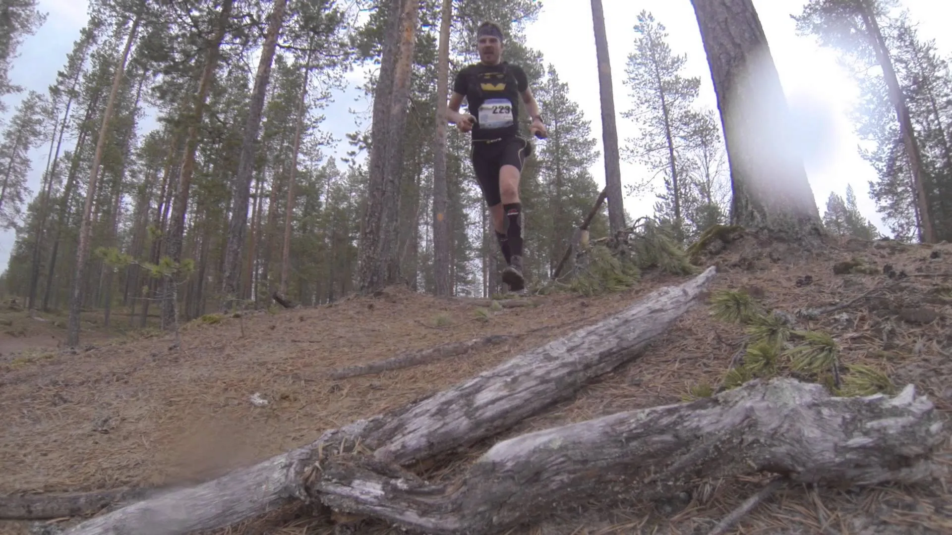 The image shows a person trail running through a forest. The runner is wearing a