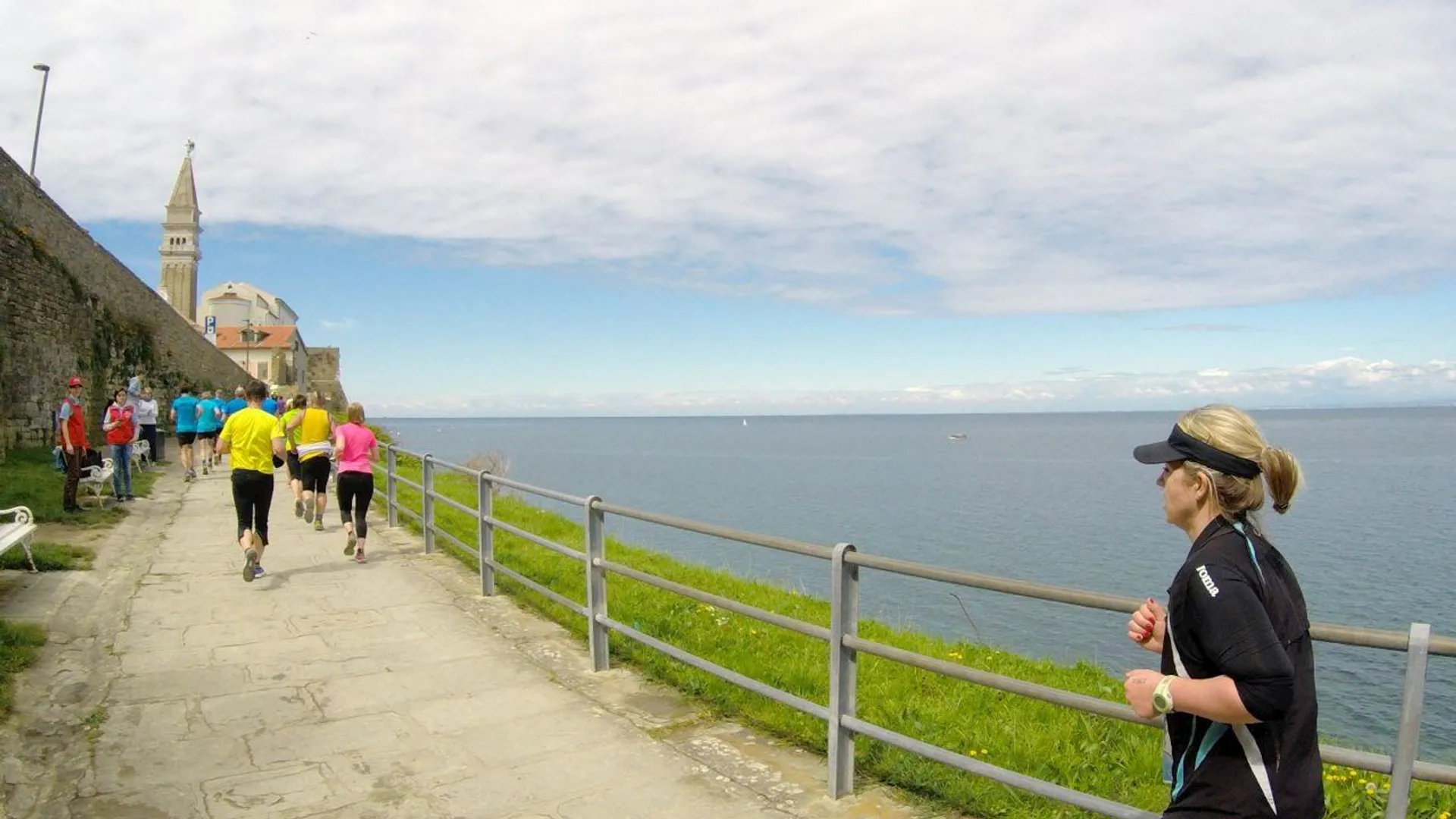 In the image, there is a coastal scene with multiple people engaged in running.