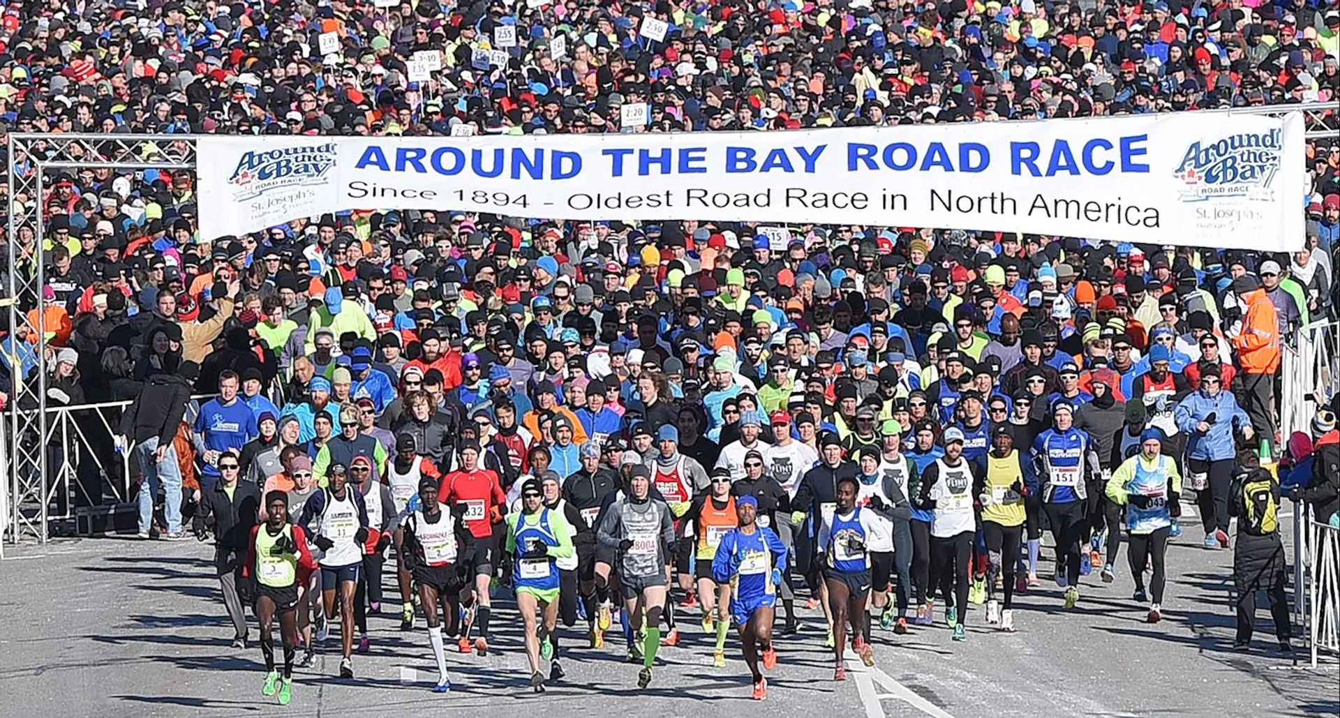 The image shows a large group of runners participating in a road race. They are