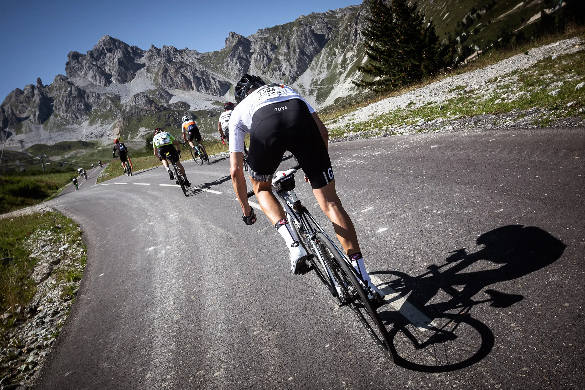 The image depicts a group of cyclists riding on a road with a mountainous backdrop