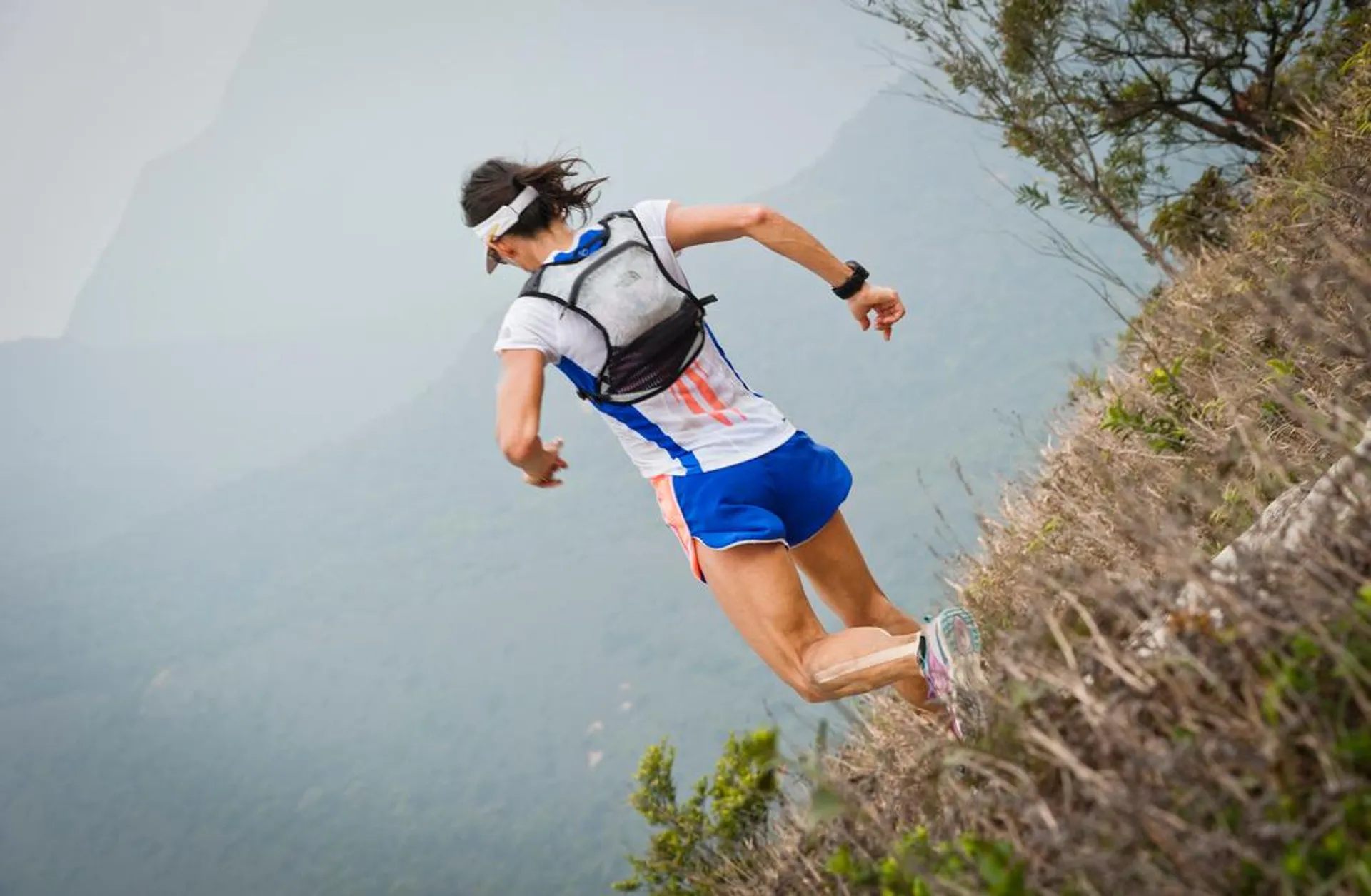 The image shows a person trail running through a natural, rugged environment. The runner