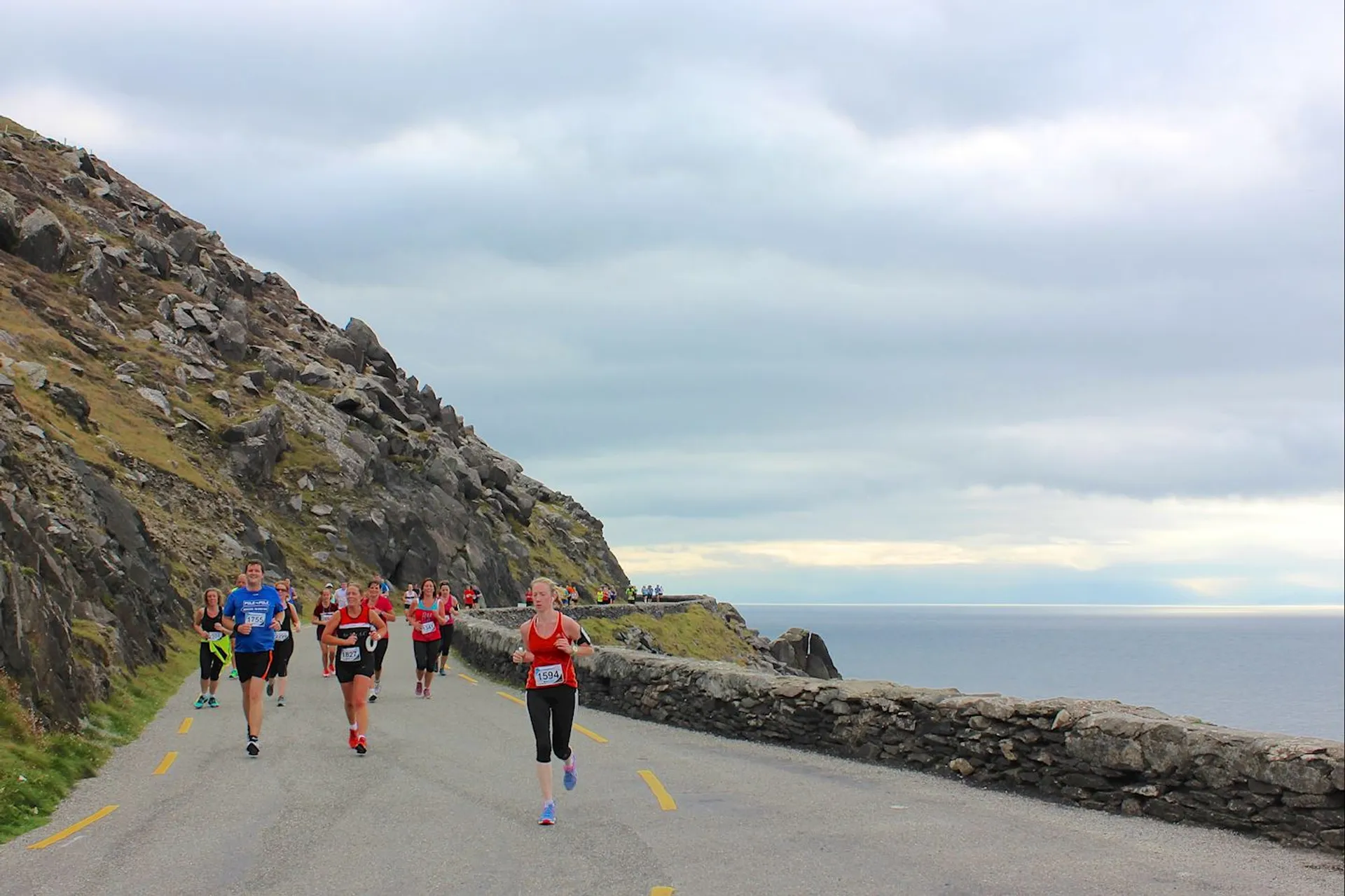 The image shows a group of runners participating in a road race along a coastal route