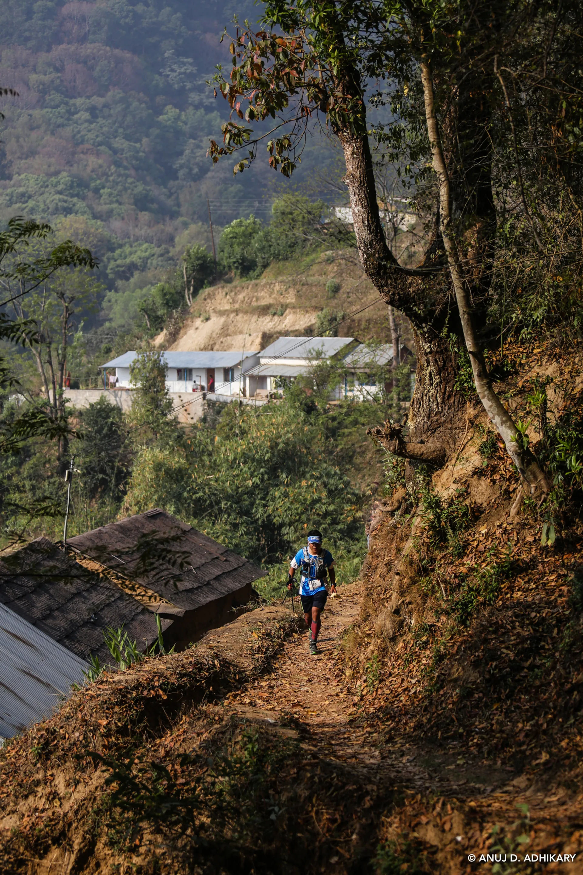 The image shows a person hiking on a narrow trail through a hilly area.