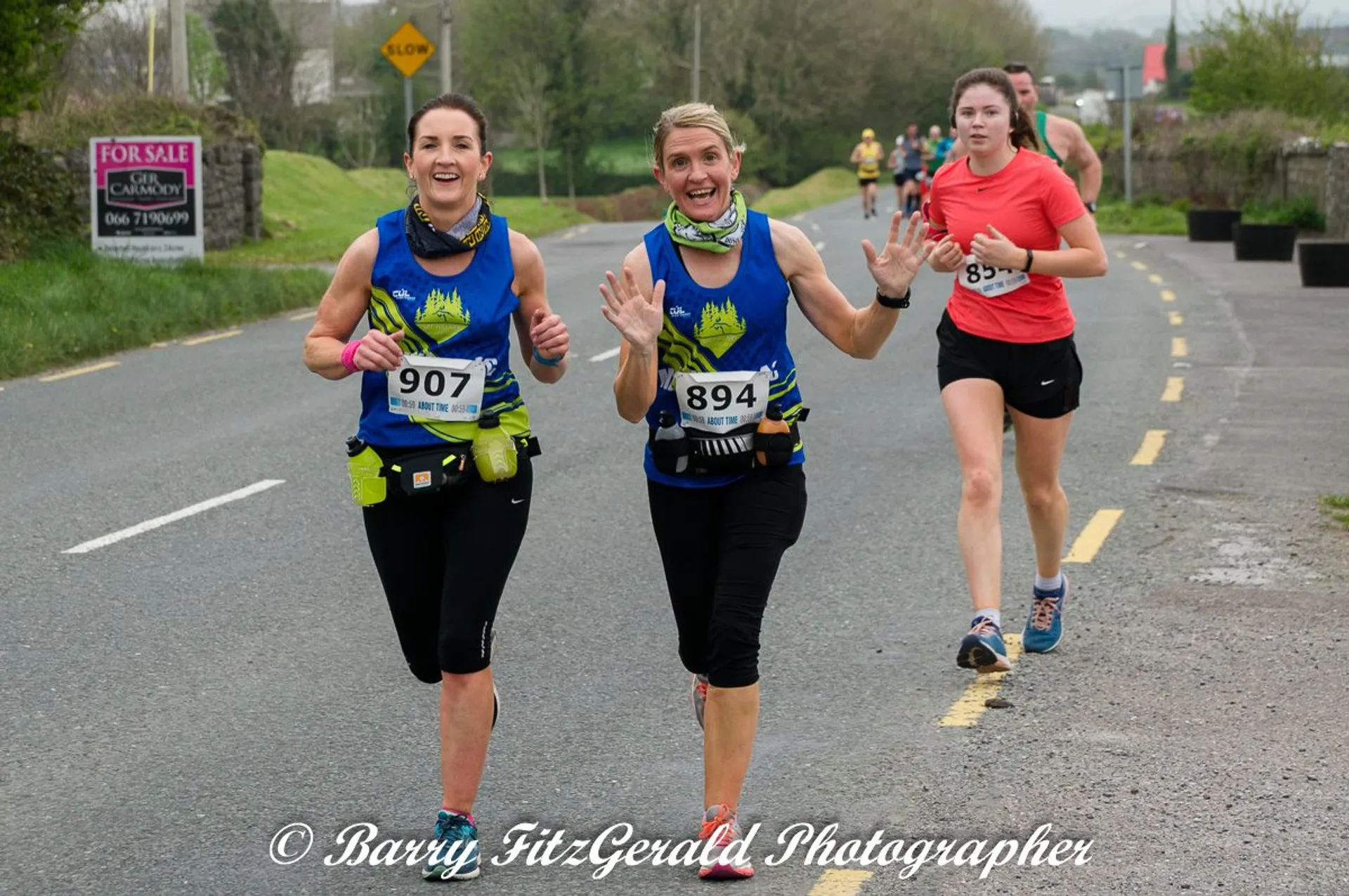 The image depicts three individuals participating in a road running event. Two women in the