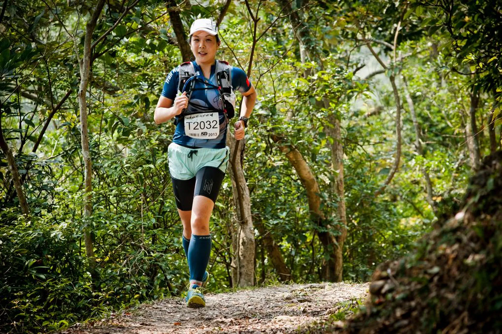 The image shows a person trail running through a wooded area. The runner is wearing