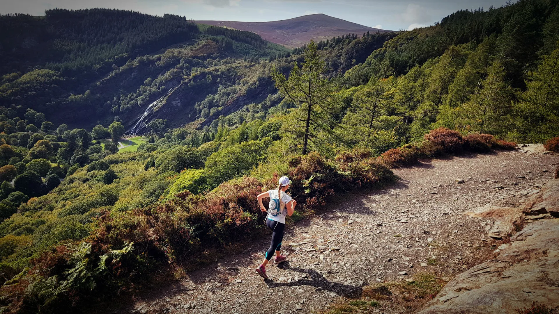 The image depicts a person hiking on a dirt trail. The hiker is dressed