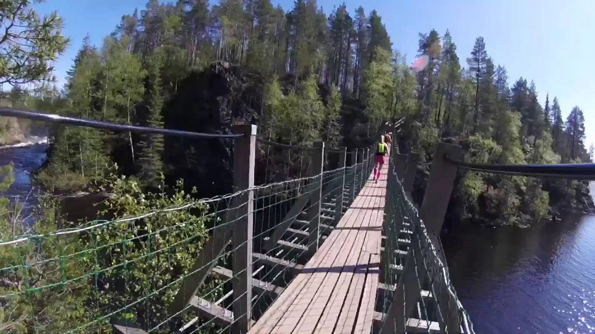 The image shows a suspended footbridge over a river or body of water. The