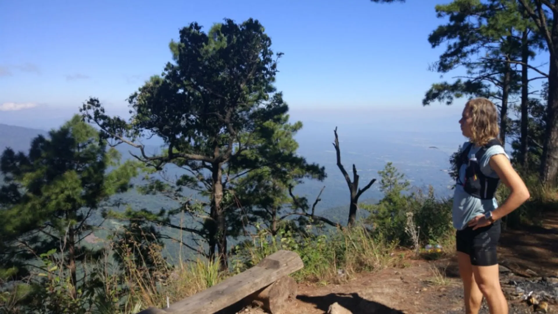 The image shows a person standing at a viewpoint overlooking a natural landscape. The person
