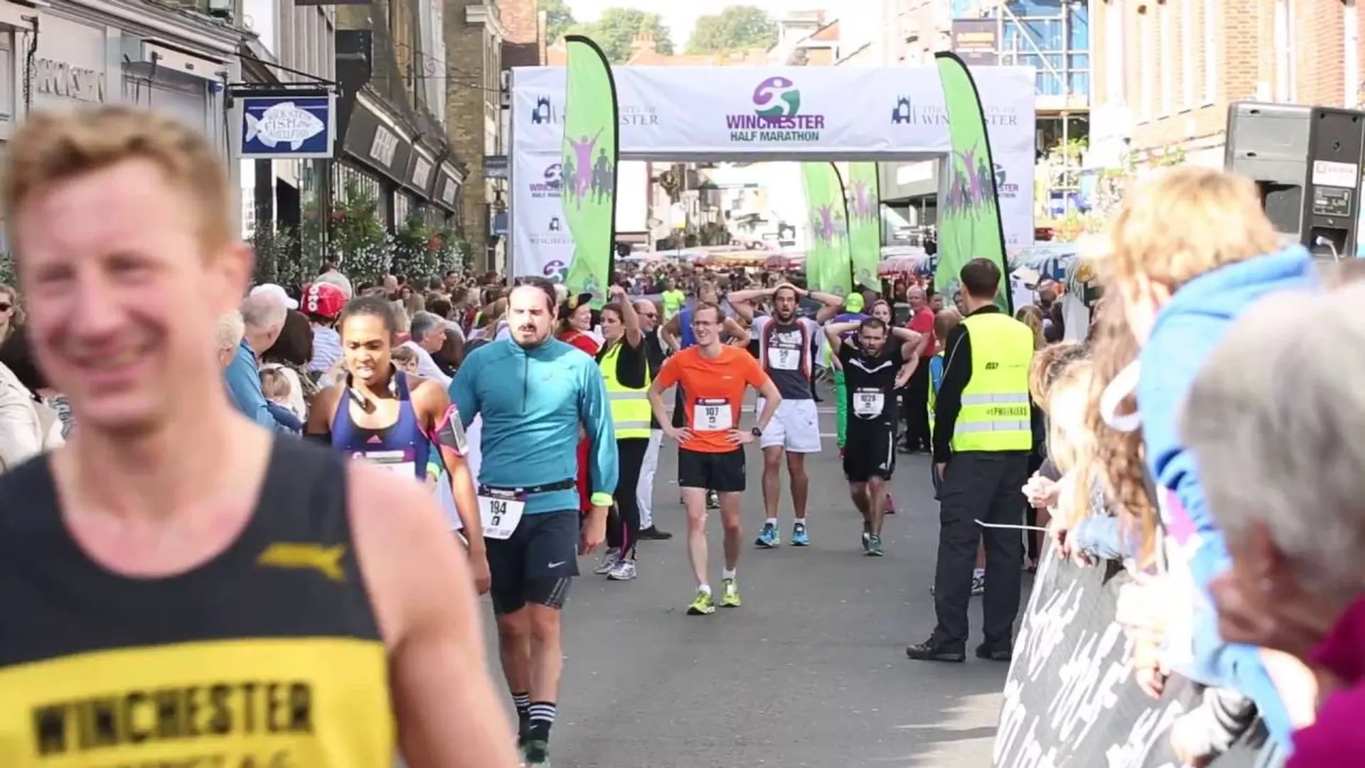 The image shows a street scene from a running event. There are multiple participants visible