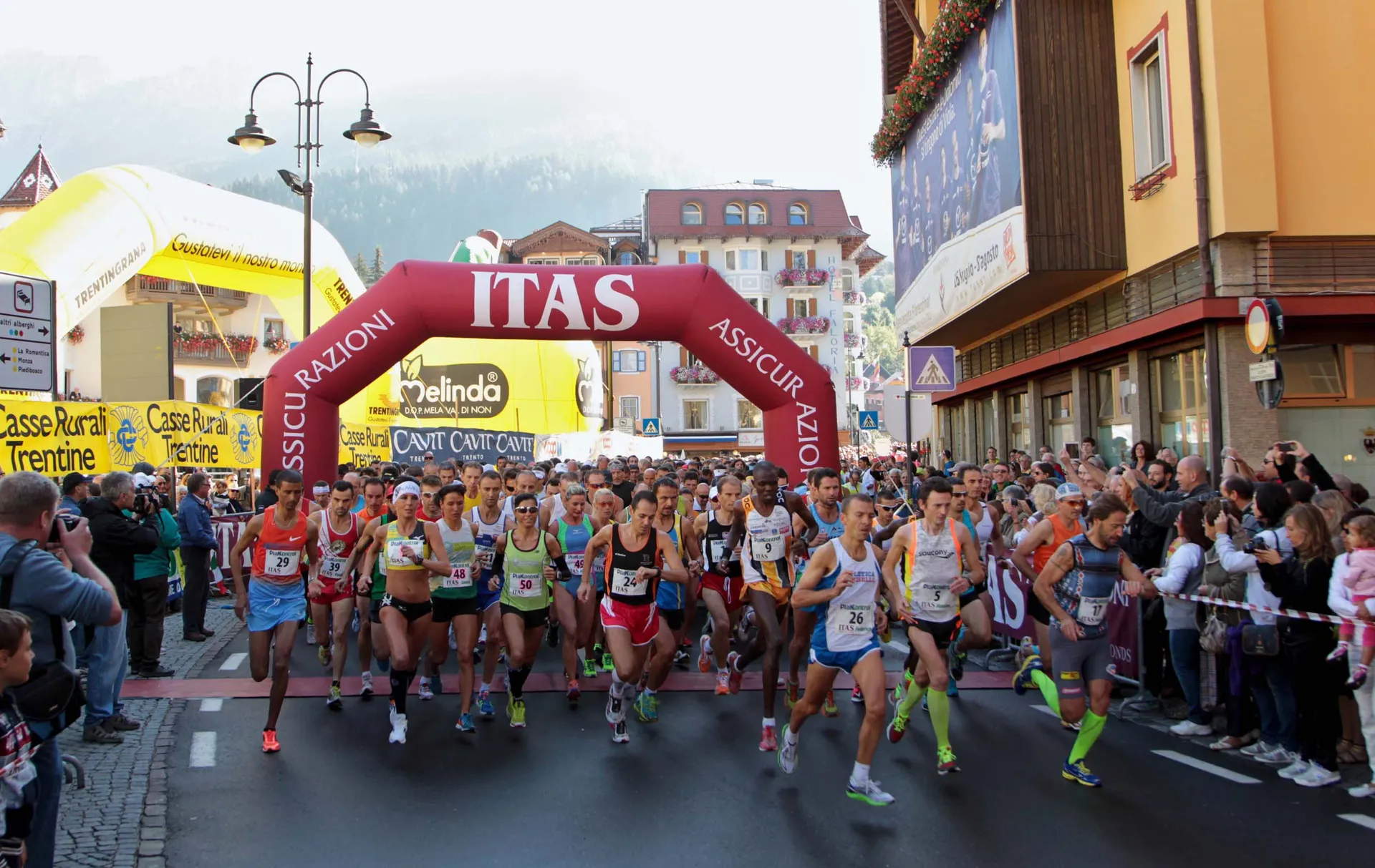 The image shows a large group of runners at the start of a road race.
