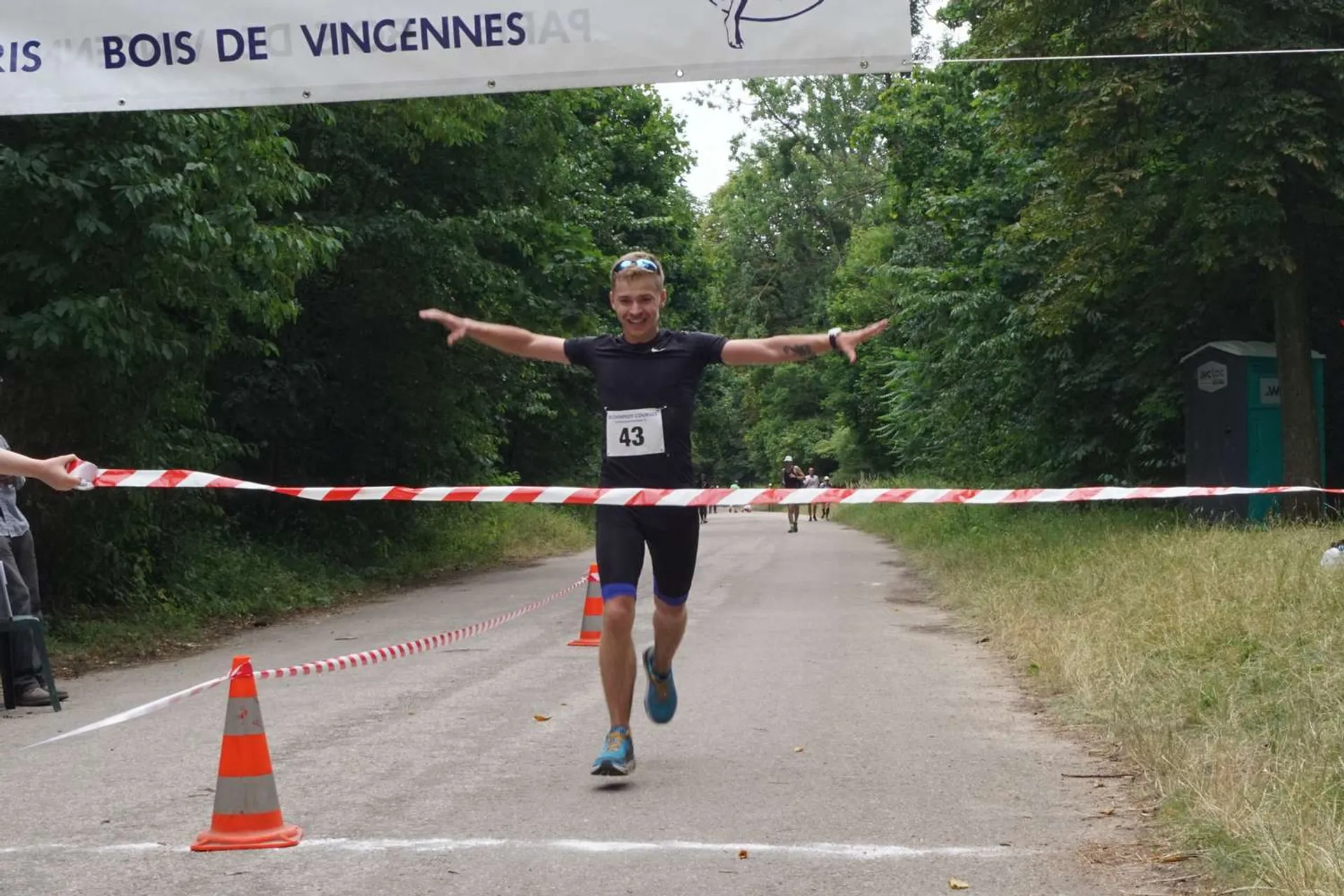 The image shows a person crossing the finish line of a race with a joyful and