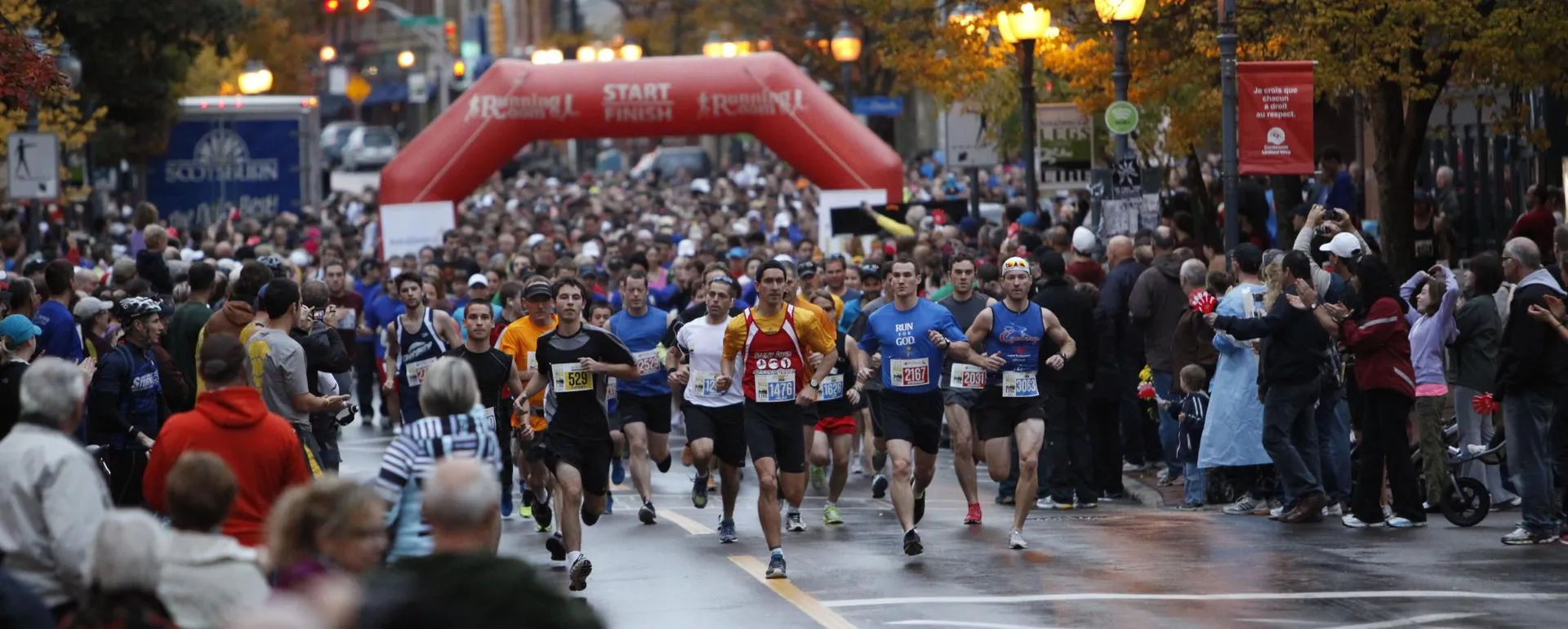 The image depicts a large group of participants at the start of a road race,