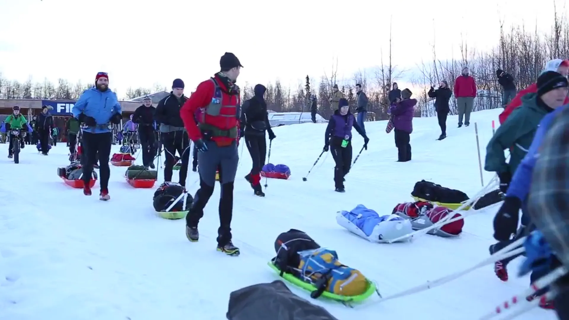 The image shows several people outdoors in a wintry environment, possibly at the start