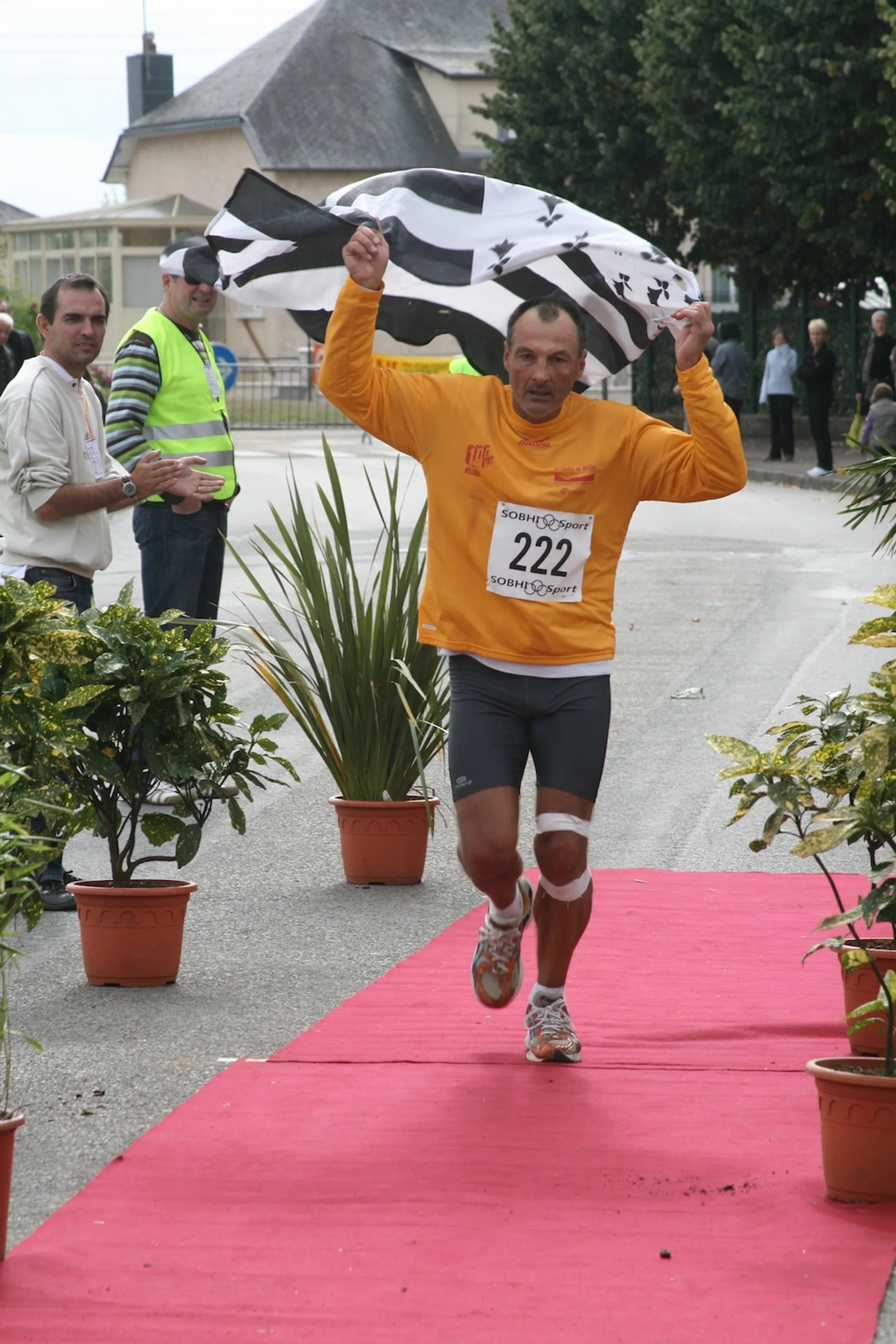 The image shows a male athlete crossing a finish line marked by a red carpet.
