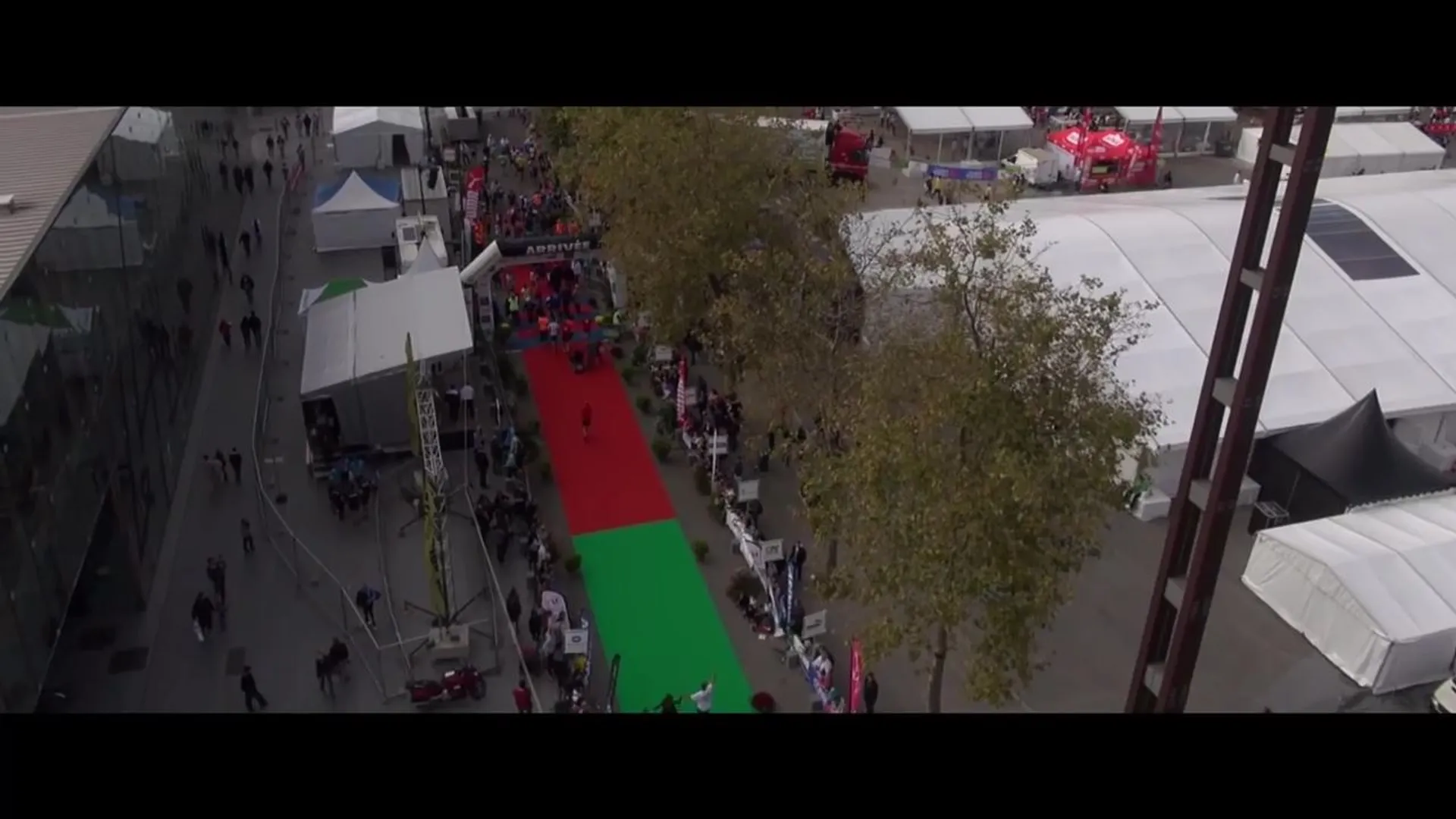 The image depicts an aerial view of an outdoor event with several white tents and a