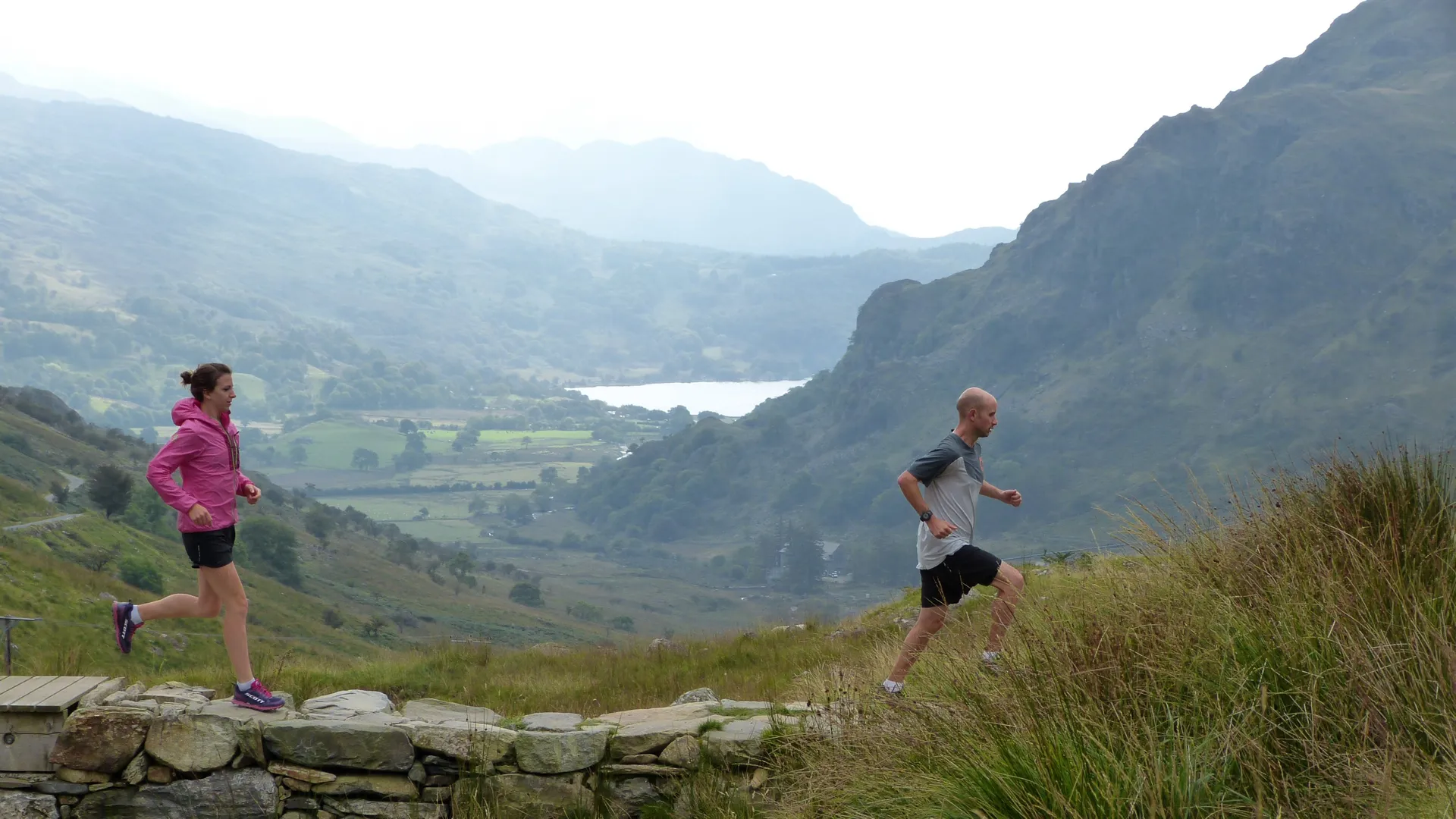 The image shows two people engaged in outdoor exercise with a scenic backdrop. The person